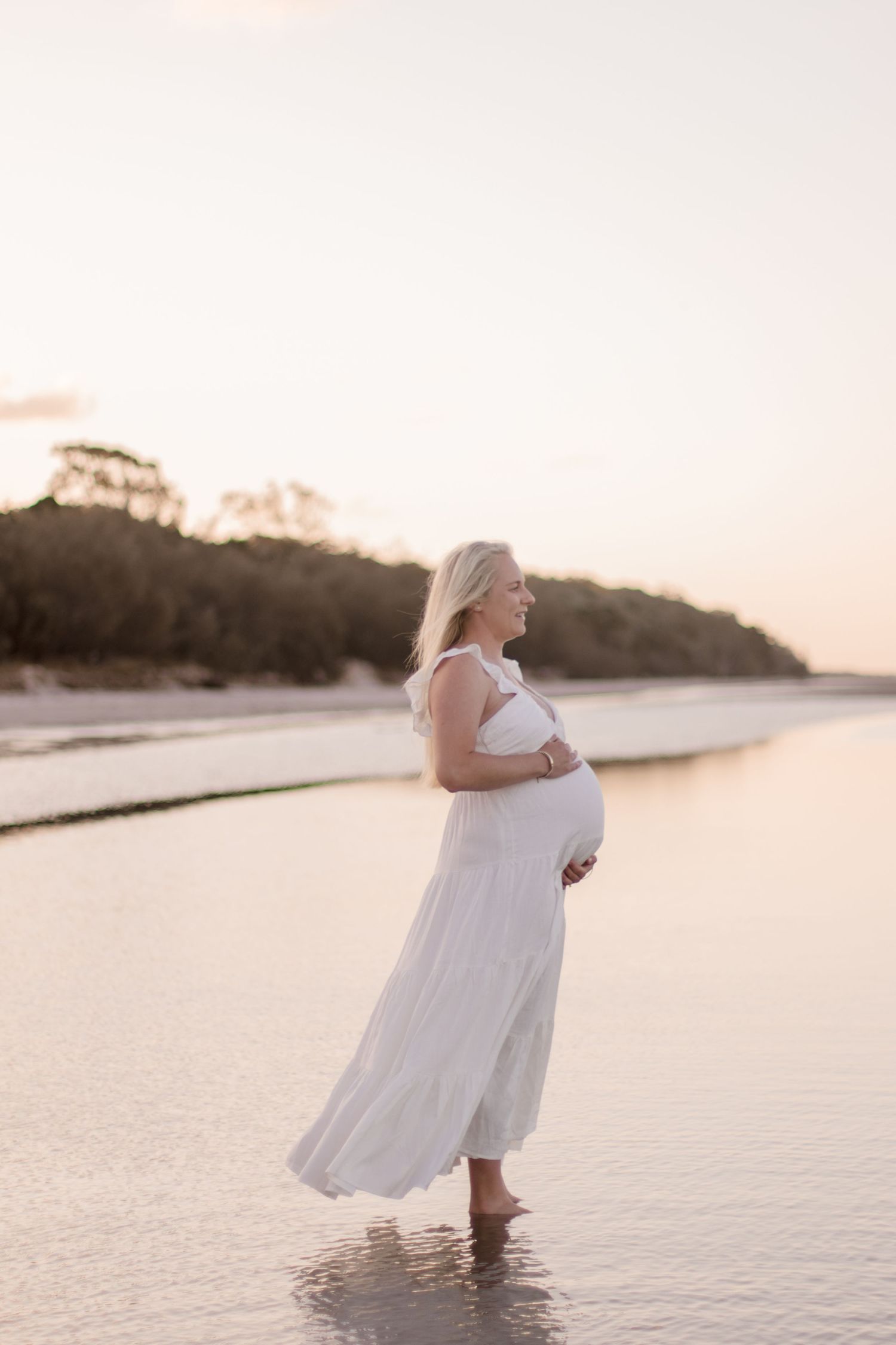 An expectant mother stands in shallow water during sunset for her beach maternity photos.