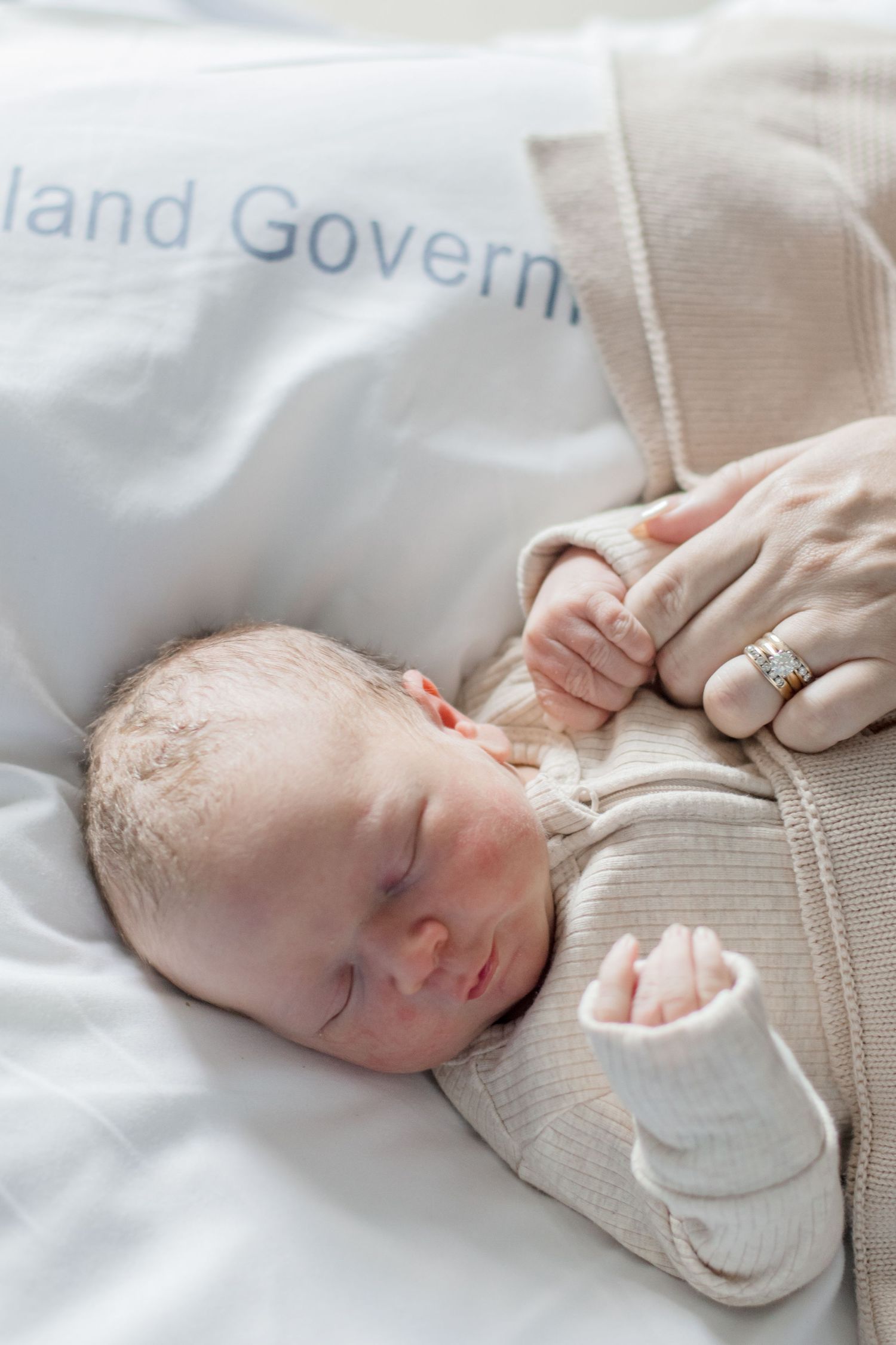 A peaceful sleeping newborn in cream knitwear resting against hospital bedding.