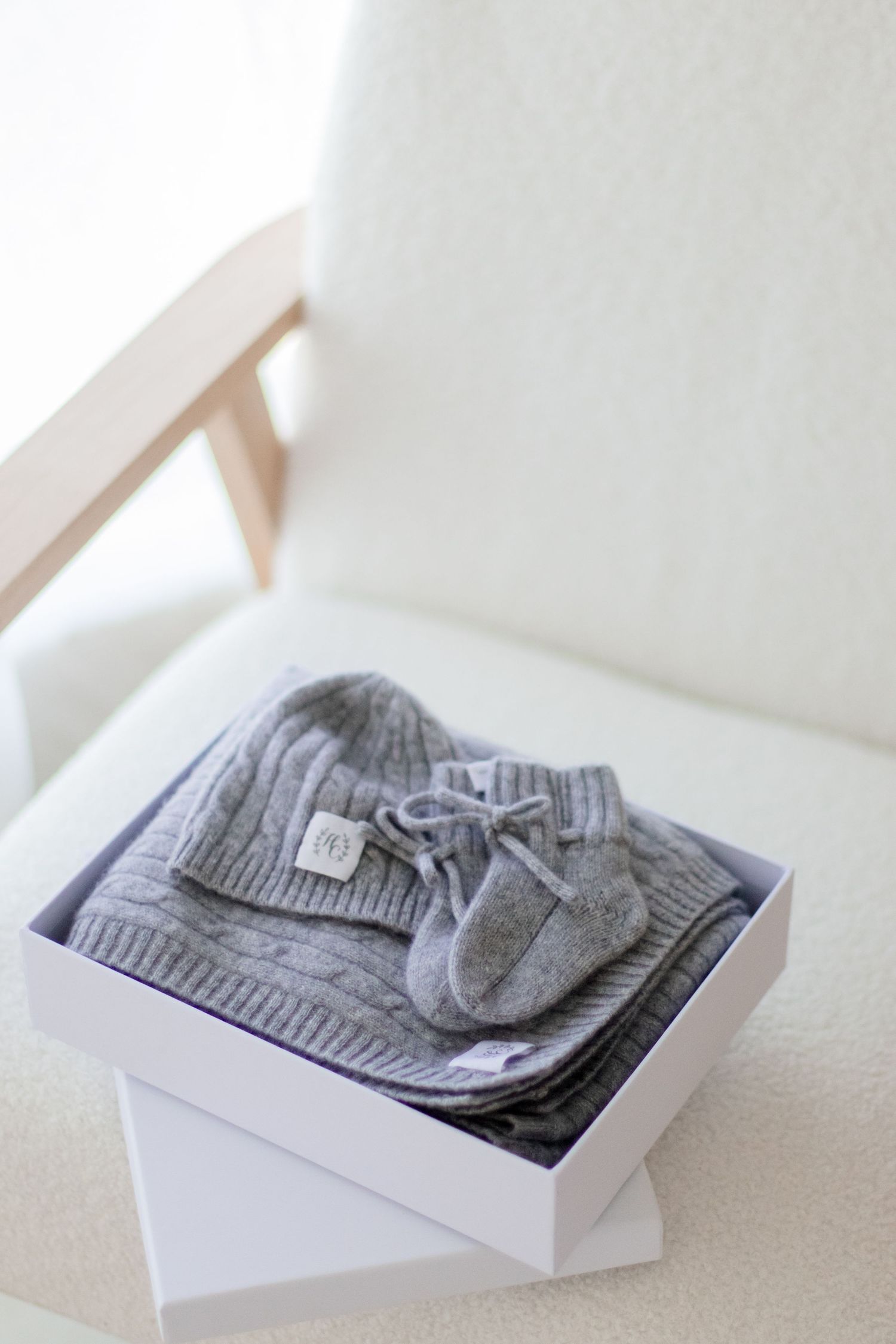 A grey knit baby beanie and booties set neatly arranged in a white gift box.