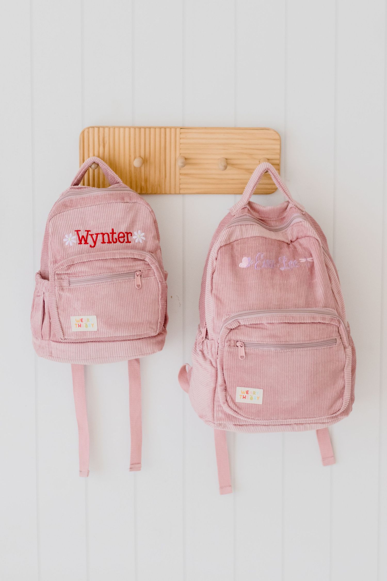 Pink mini backpacks displayed in descending size order against a white wall, showing gradual size progression.