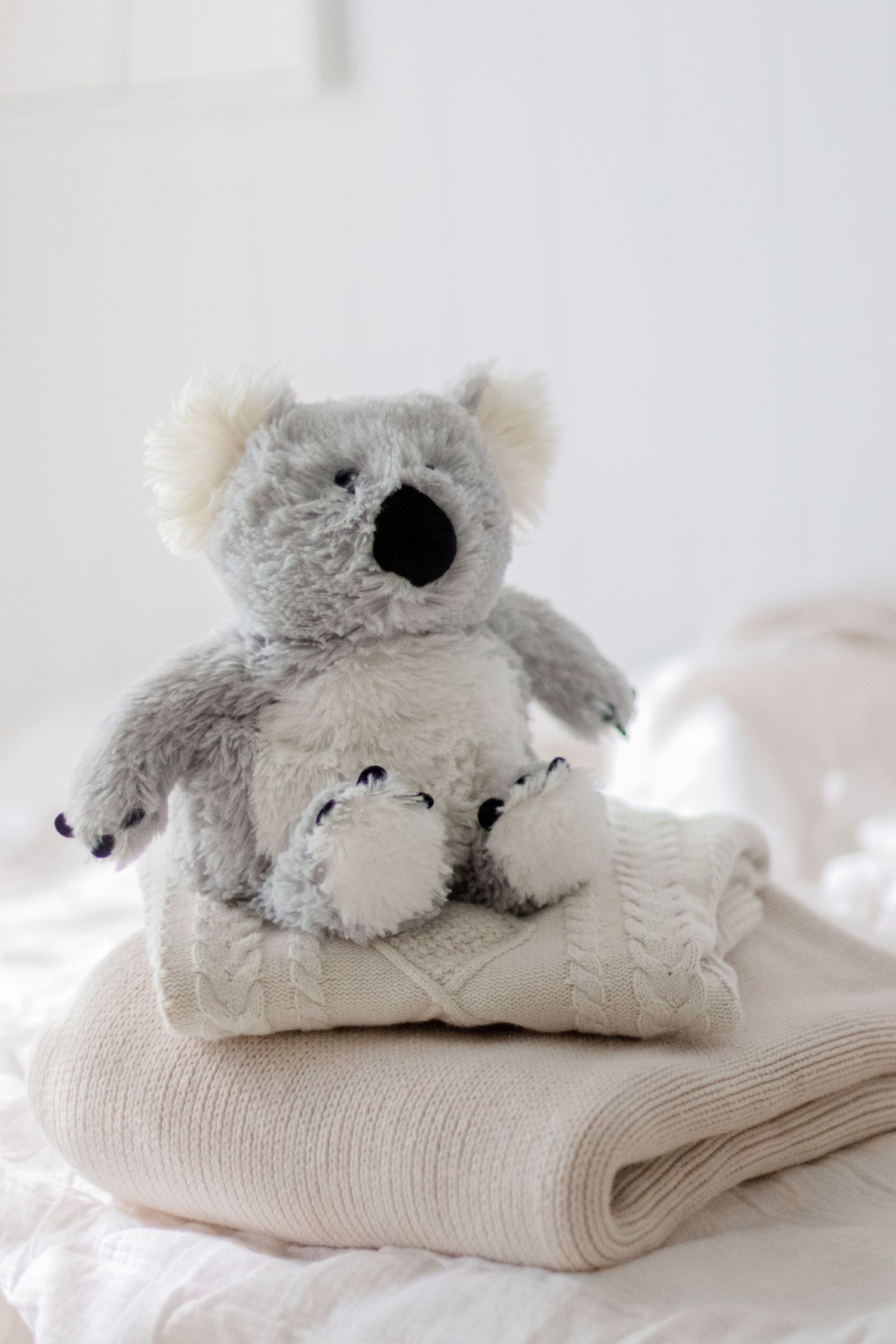 Gray plush koala toy resting on folded cream-colored knit fabric in soft natural lighting.