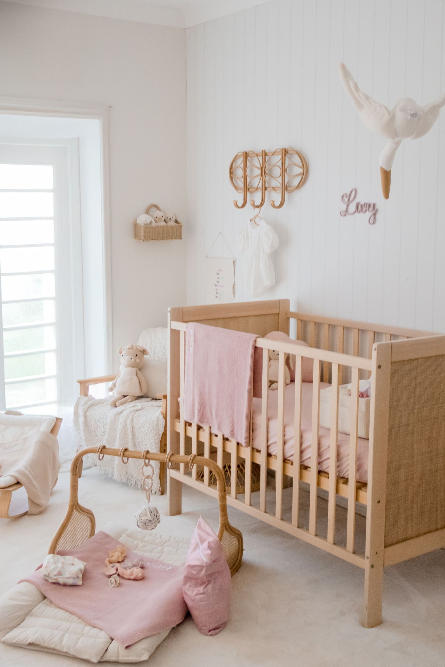 A serene nursery decorated in neutral tones with a wooden crib, pink decor accents, and minimalist wall art.
