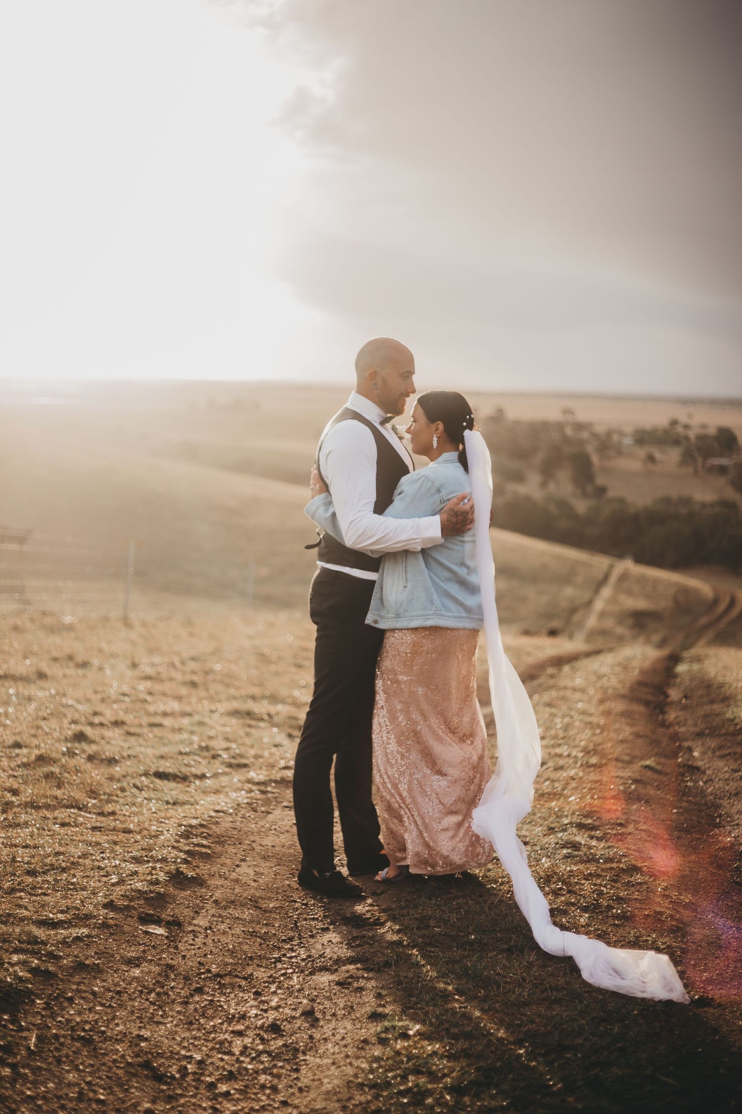 A romantic sunset moment shows a couple embracing on a hilltop path with a flowing white veil catching the golden light.