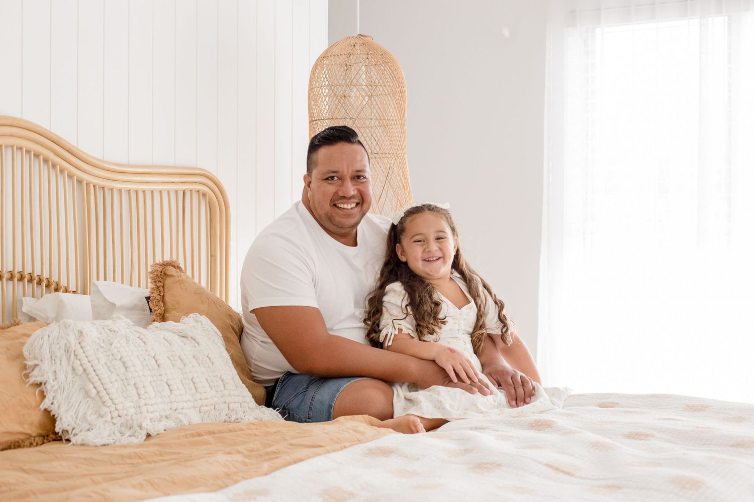 Parent and child share happy moment while sitting on wooden bed with rattan headboard.