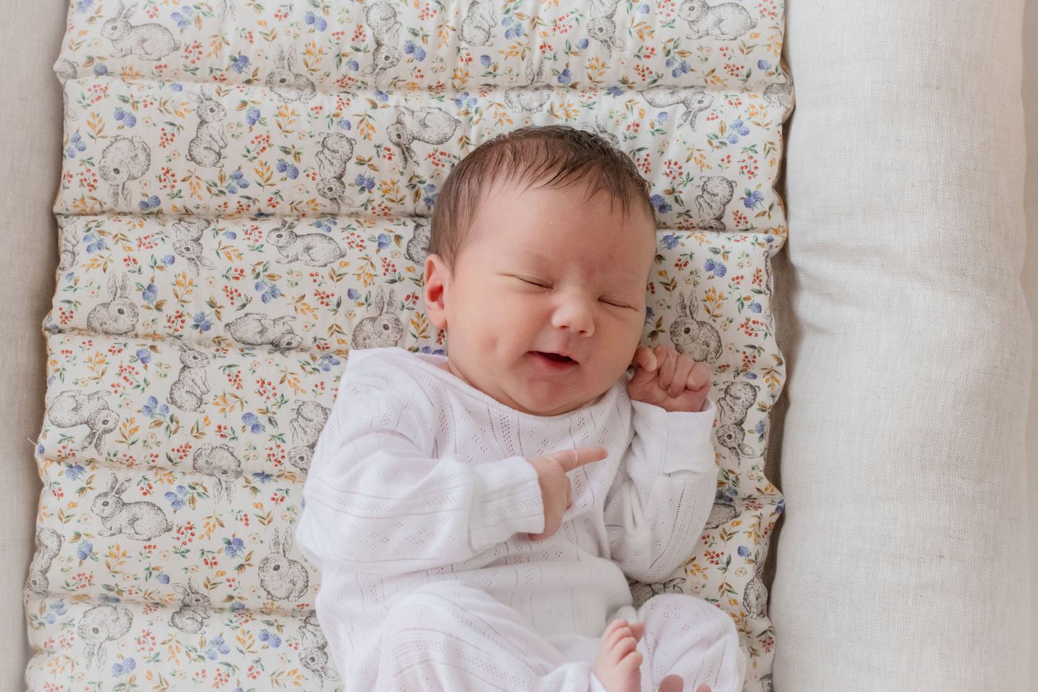 Infant wearing white outfit rests on floral patterned bedding while sleeping peacefully.
