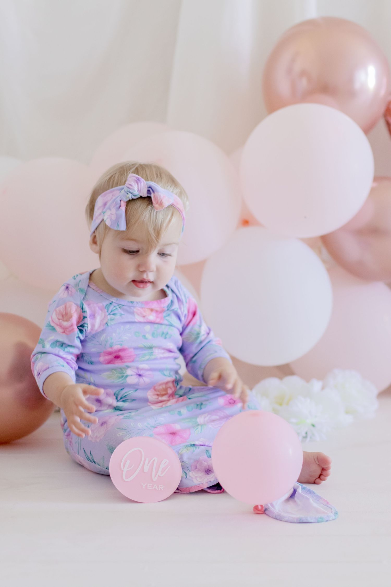 A small child in floral sleepwear looking down at pink balloons during a photo shoot.