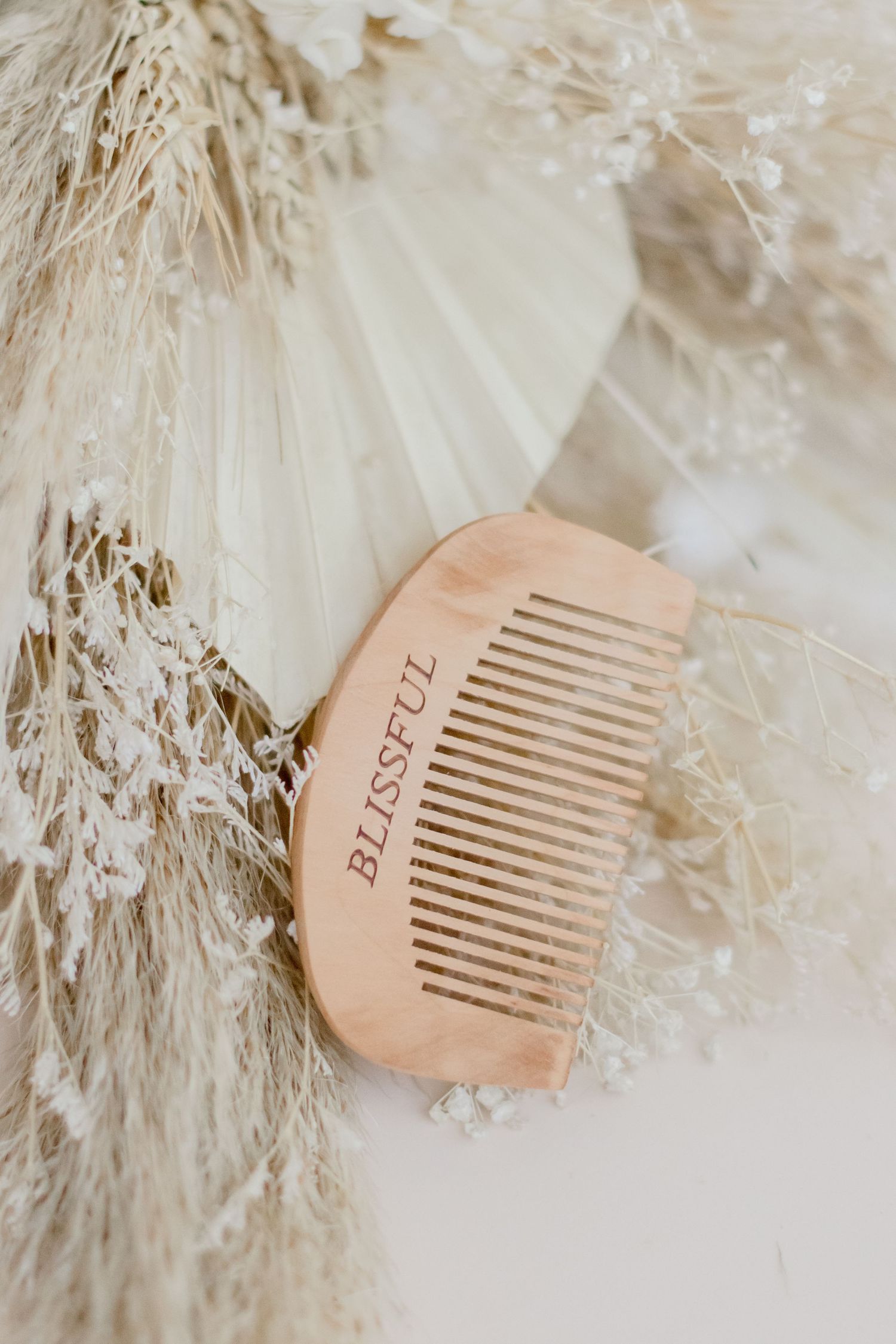 A wooden comb with engraved text displayed on a soft white feathery background in a series of three similar shots.