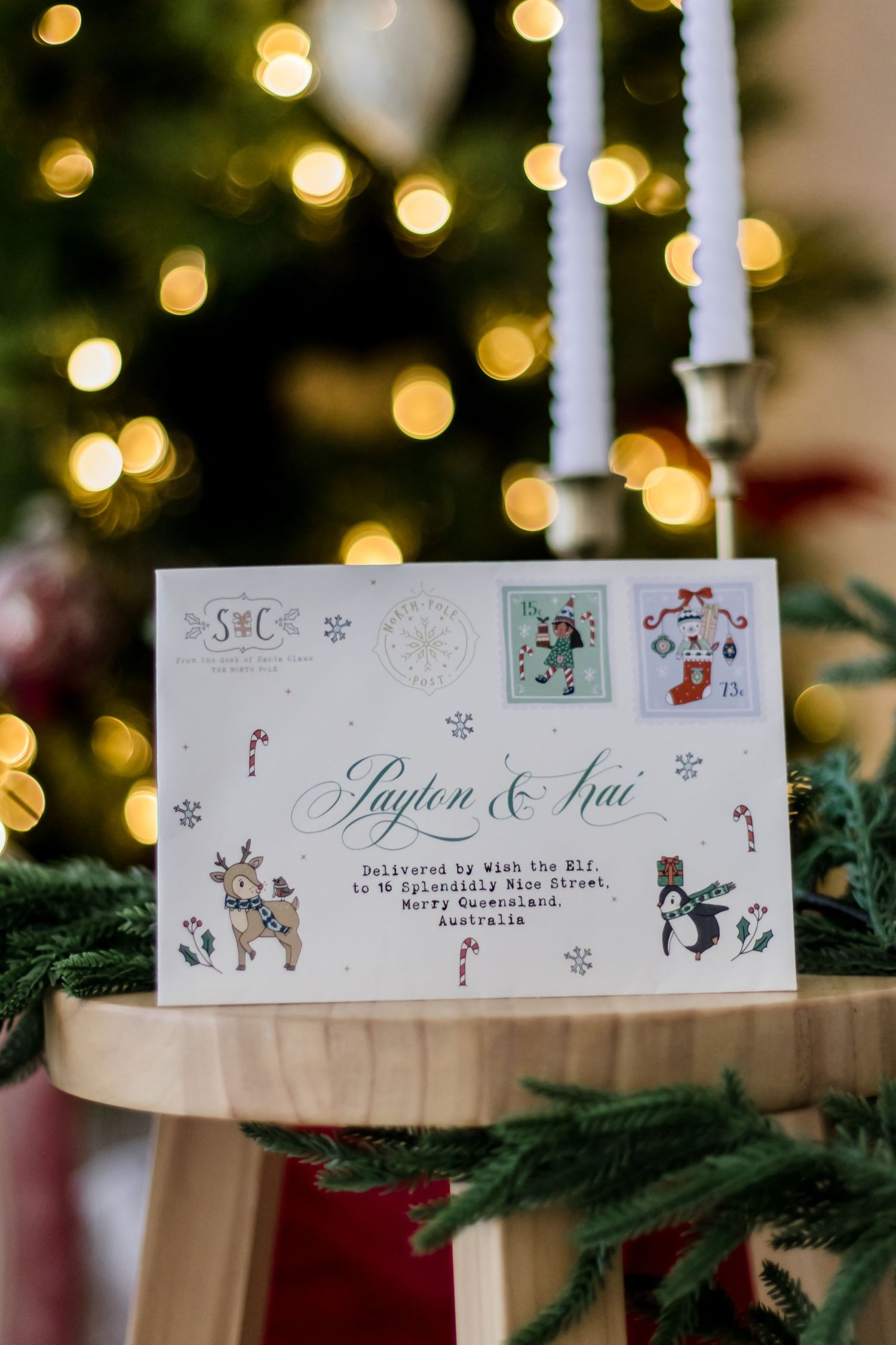 Holiday place cards with winter illustrations and names displayed on evergreen branches with twinkling Christmas lights.