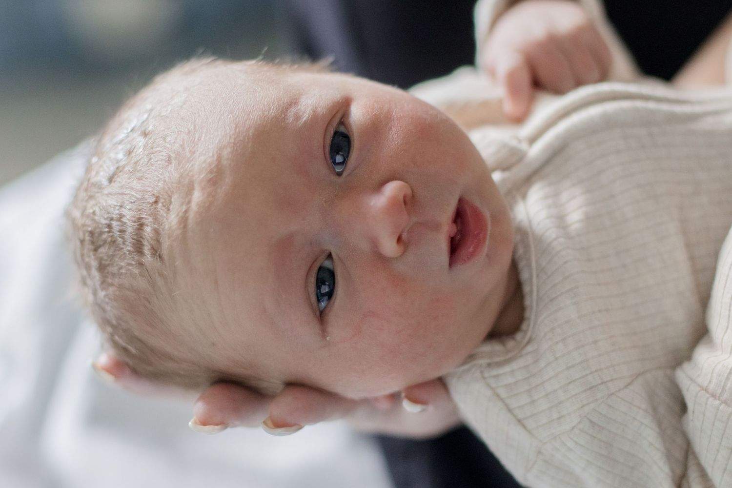 Close up of newborn with bright eyes wearing cream colored outfit.