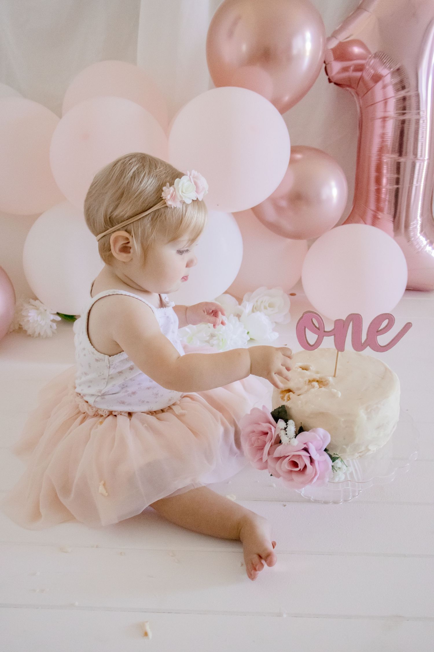 Side view of baby in tulle dress at first birthday photoshoot with cake and balloons.