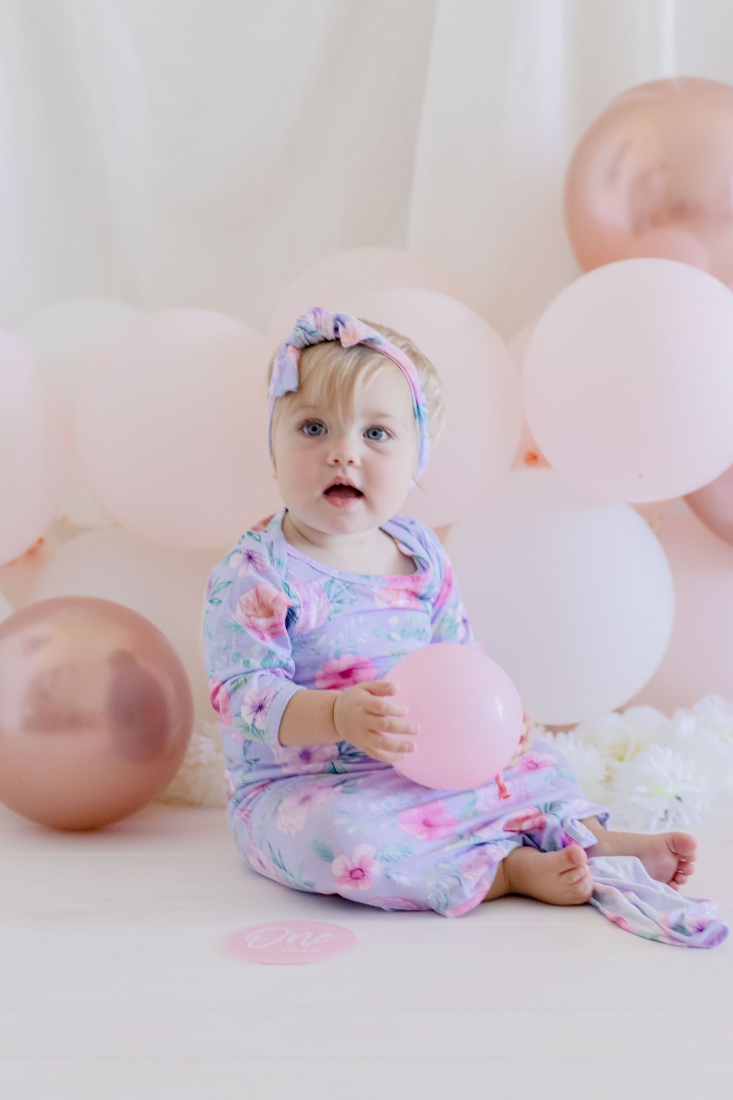 A joyful moment captured with pink balloons and floral outfit against a white backdrop.