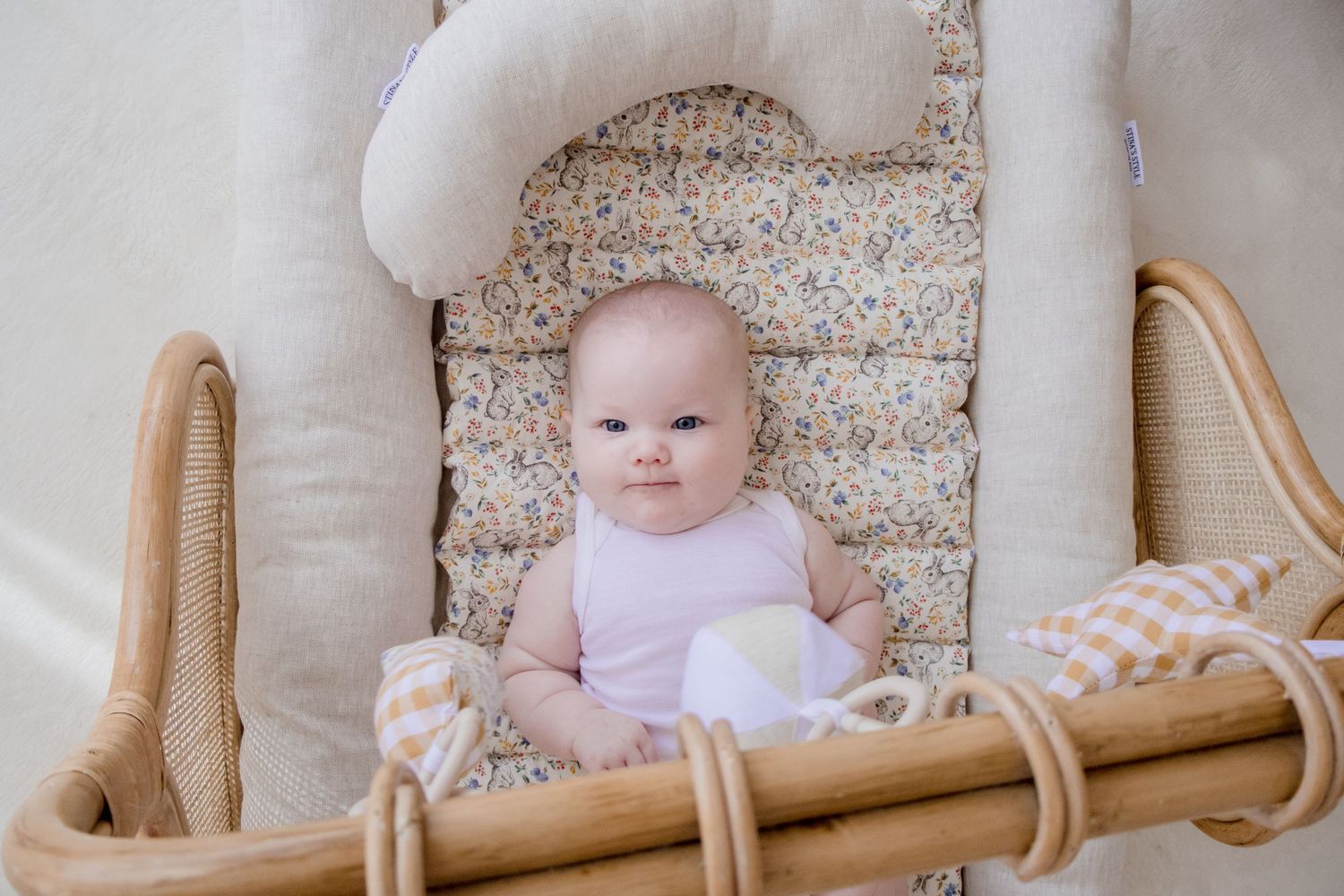 A small infant in a lavender outfit sits in a wicker bassinet with floral bedding.
