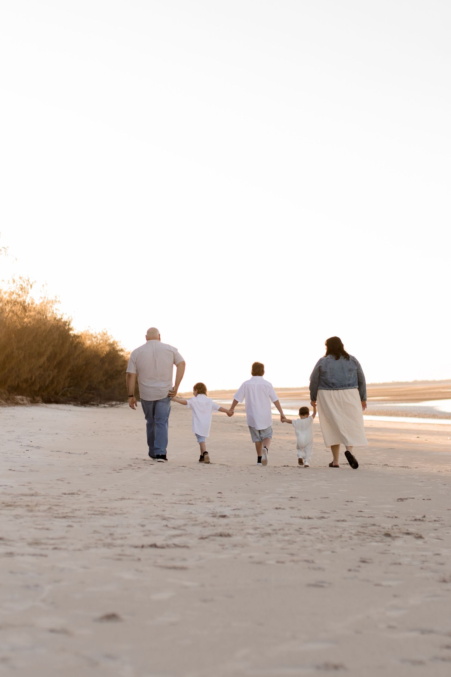 Family walking together on a sandy beach at sunset with gentle waves in the background.