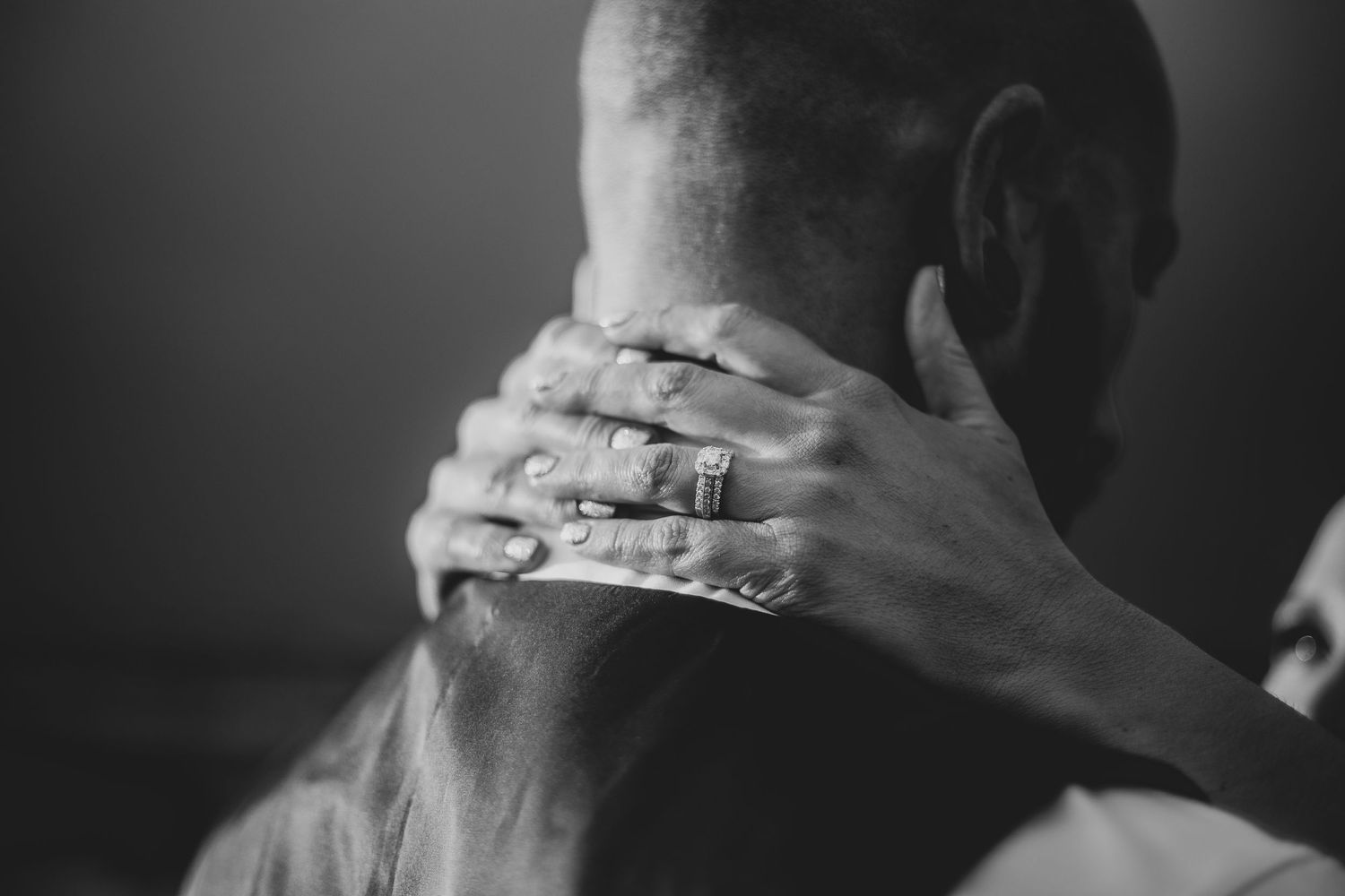 A black and white close-up photograph shows hands with wedding rings embracing in an intimate moment.