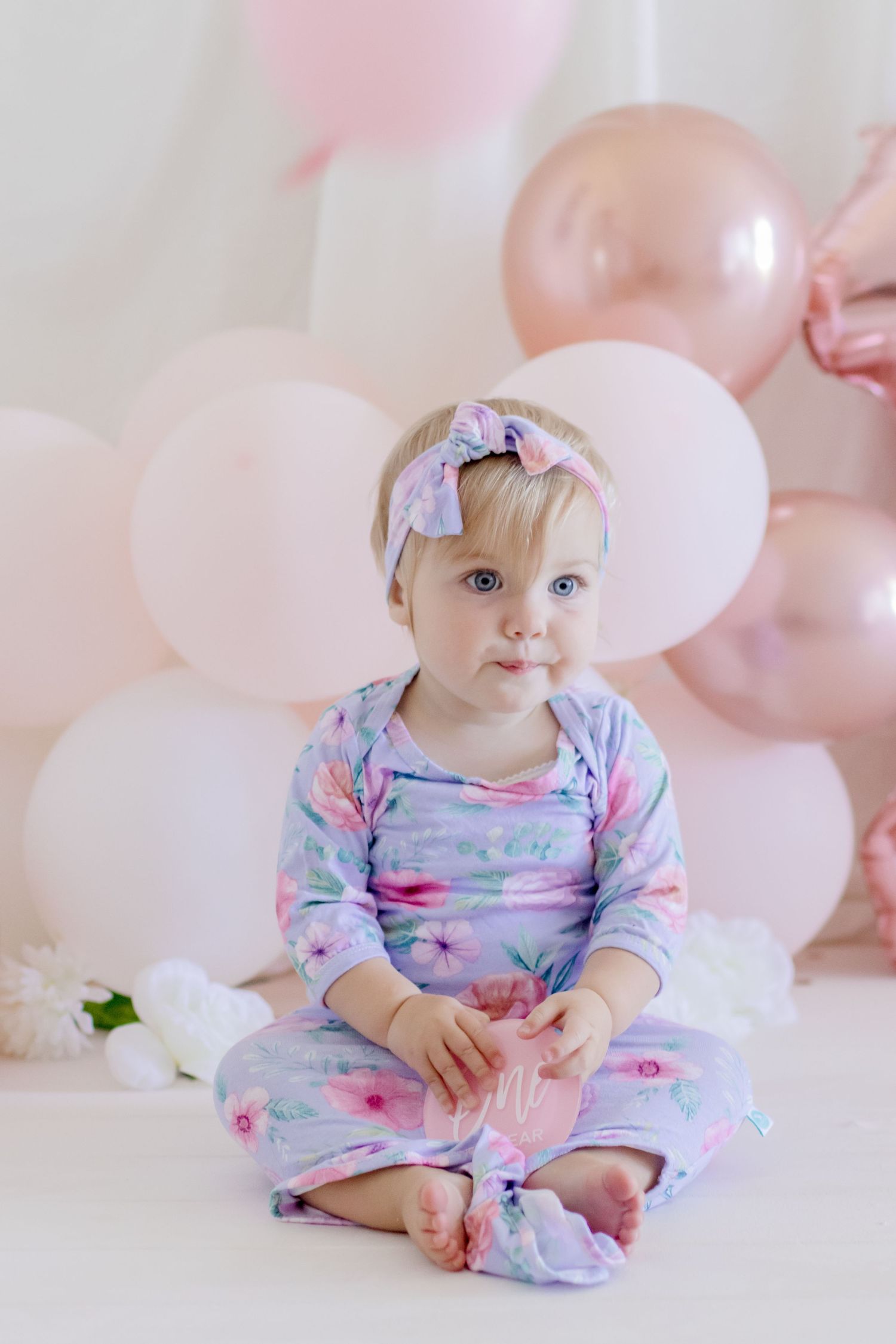 A dreamy photoshoot featuring floral prints and pink balloons in a soft white setting.