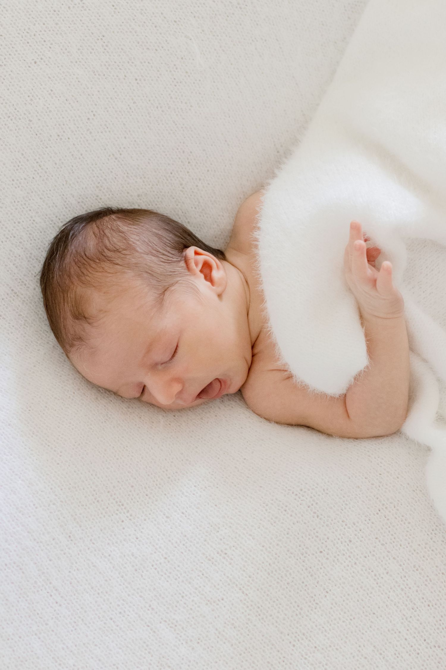 Peaceful newborn sleeps on white textured surface wrapped in soft blanket.