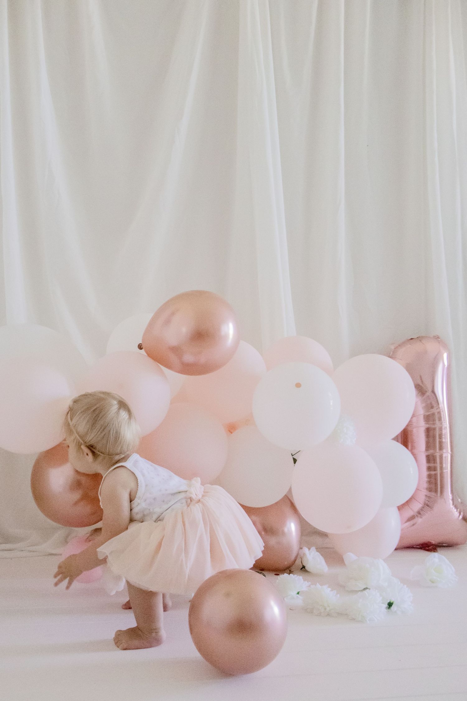 Toddler in pink tulle dress exploring balloons during a minimalist birthday photoshoot.