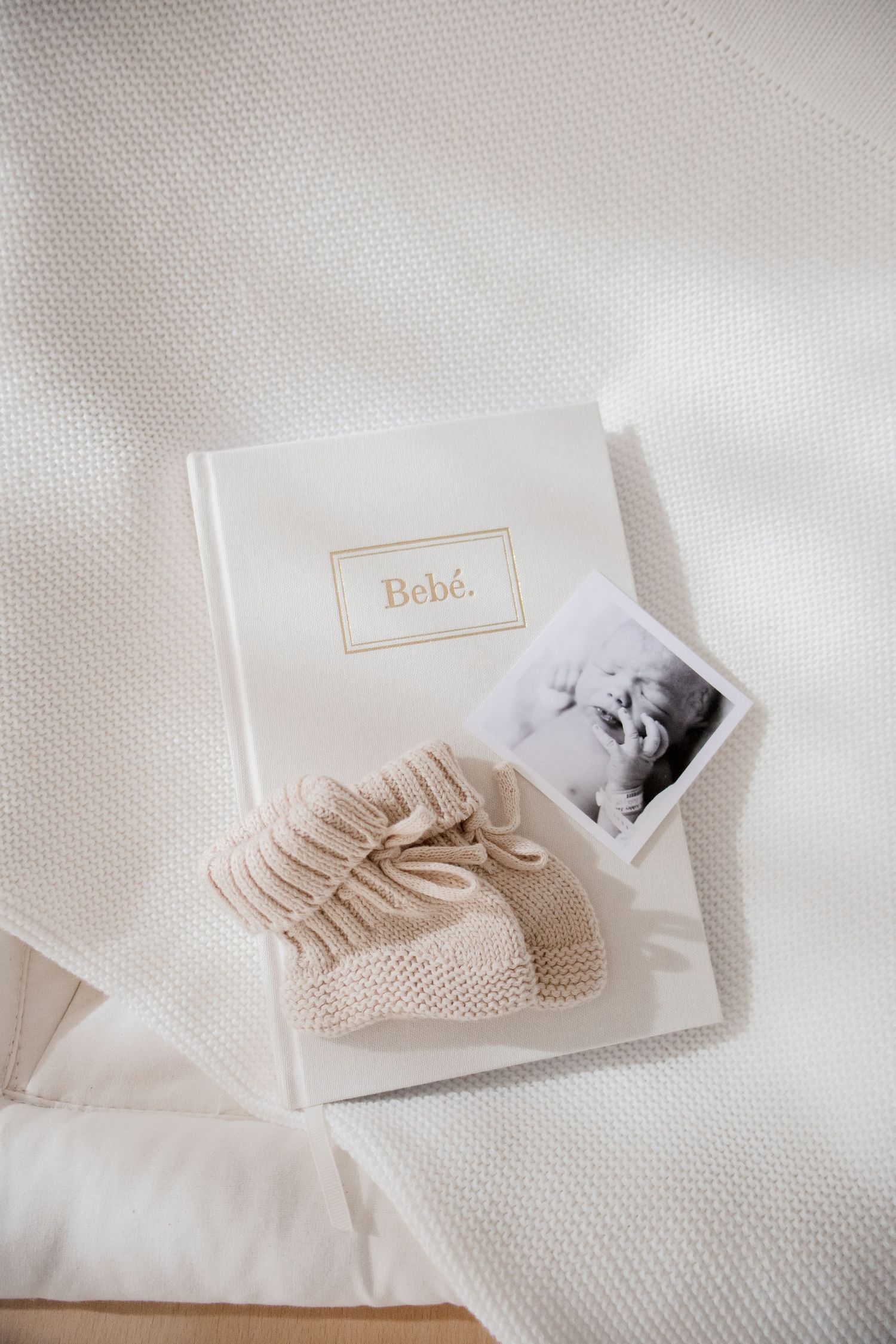 A white baby photo album with 'Bebe' text, small knitted booties, and a black and white photograph on textured fabric.
