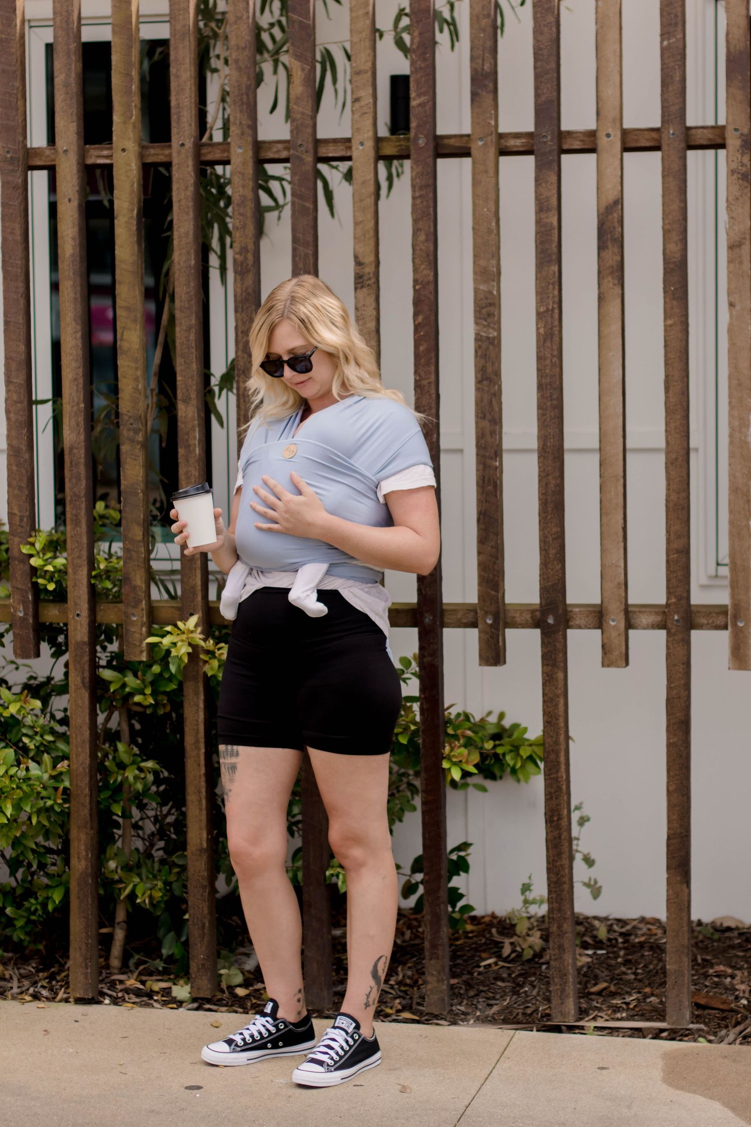 A person in black shorts and a light shirt bends down to pet a small white cat near a wooden fence.