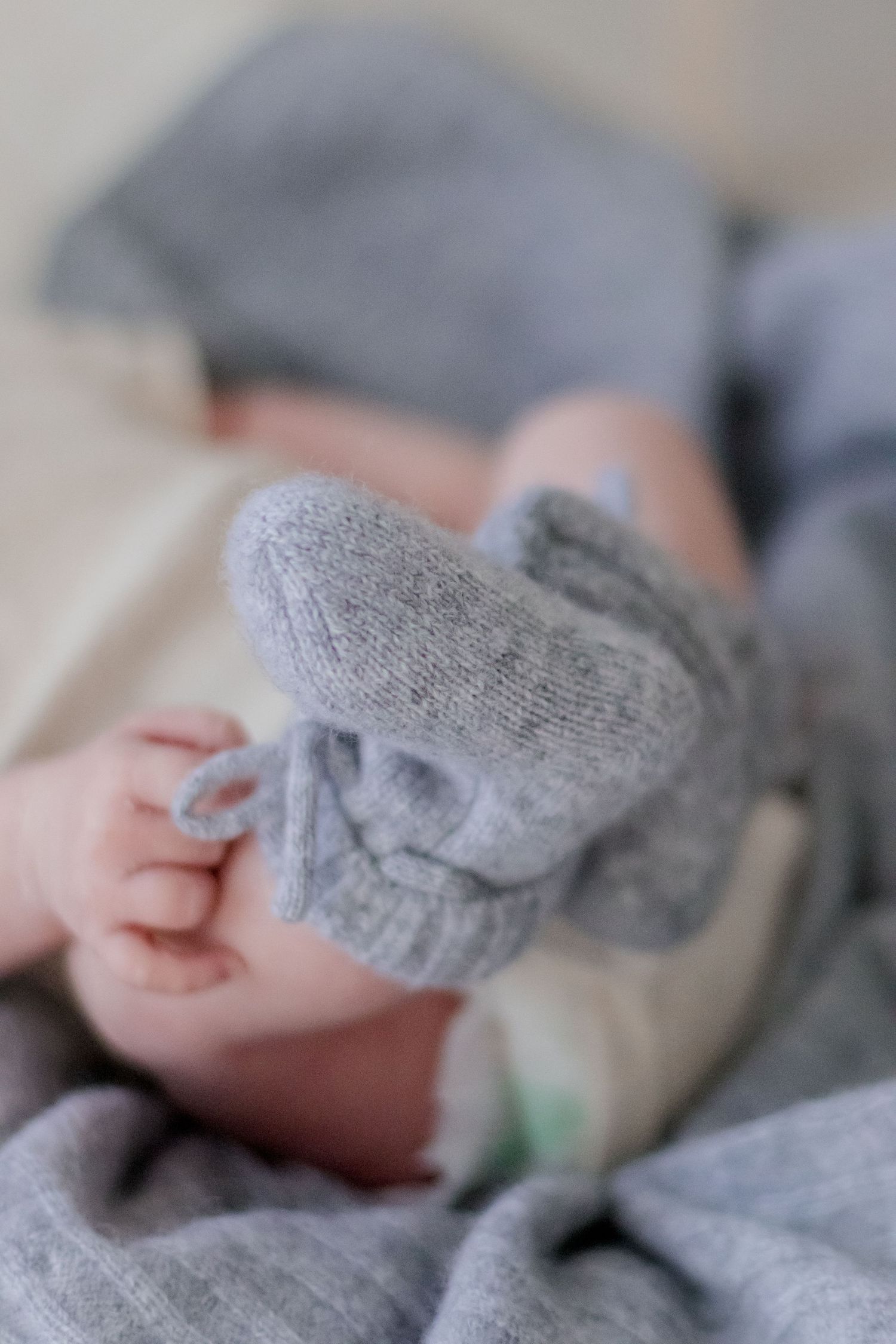 A tiny newborn hand grasps a soft gray sock against a blurred neutral background.