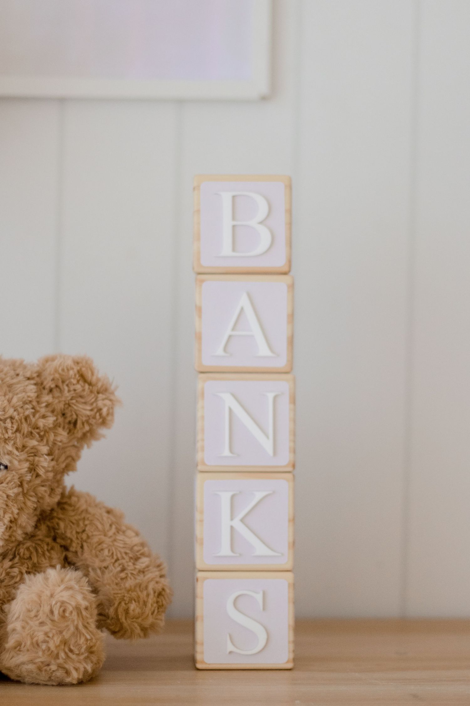 White wooden blocks spelling 'BANKS' with a partial teddy bear visible in frame.