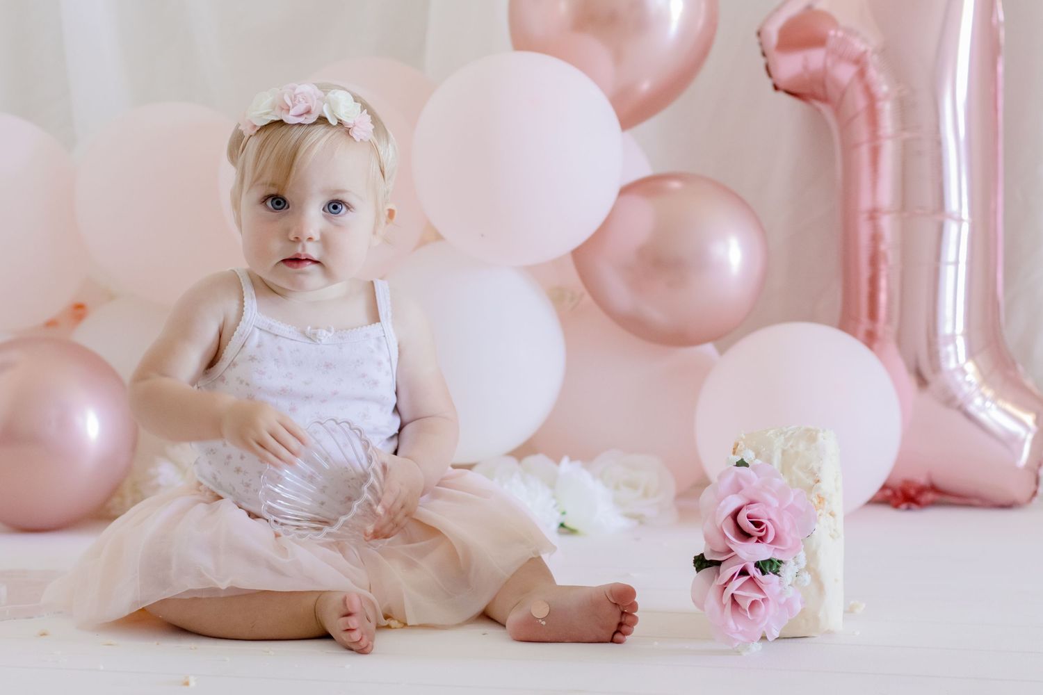 First birthday portrait with pink balloon backdrop and floral arrangements.