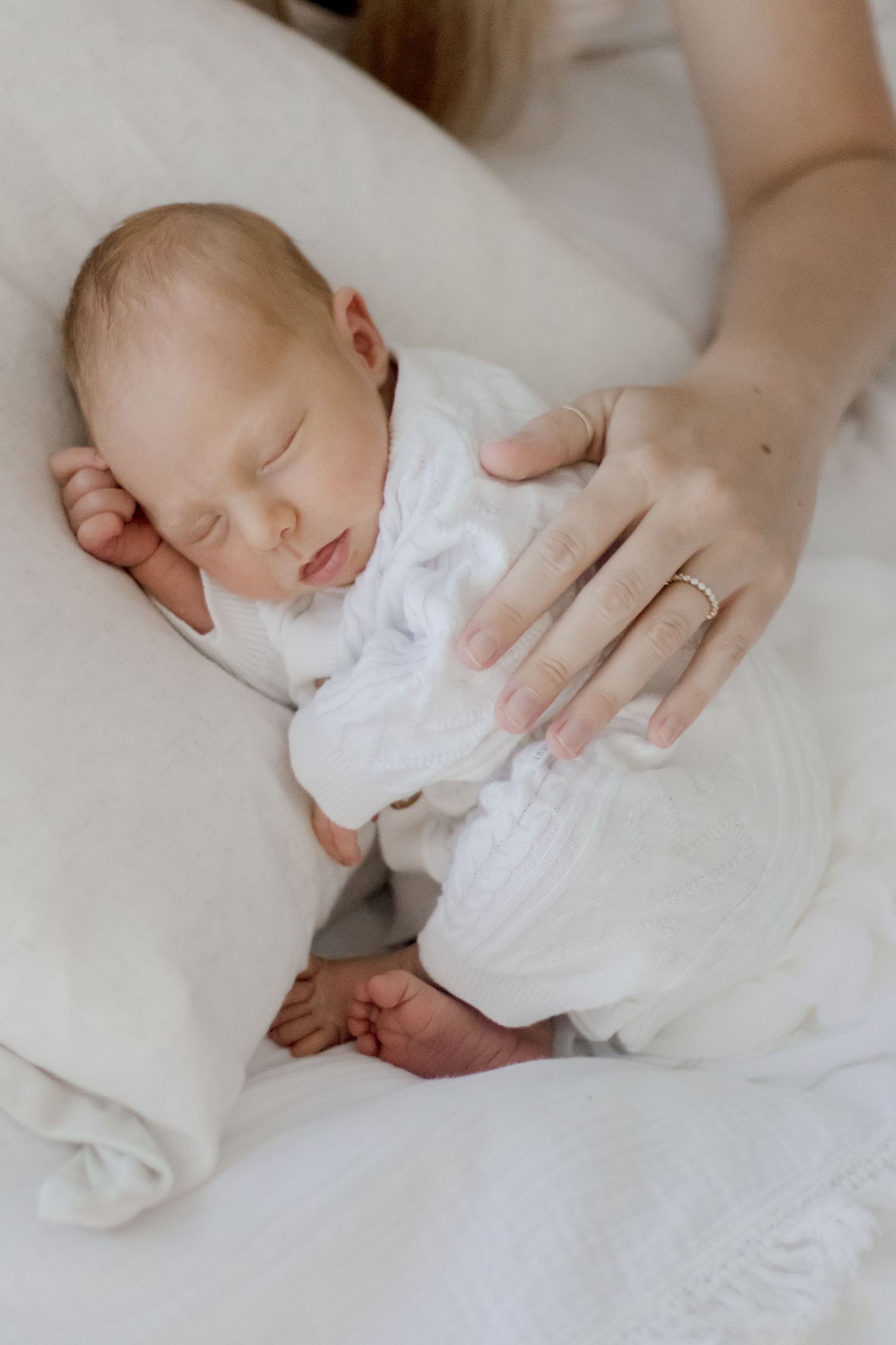 Sleeping newborn in white outfit being cradled on soft bedding.