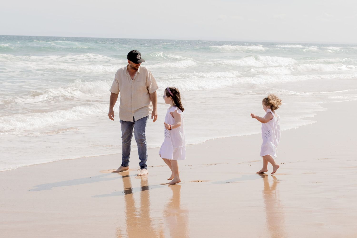 A family strolls together along the beach shoreline as waves crash behind them.