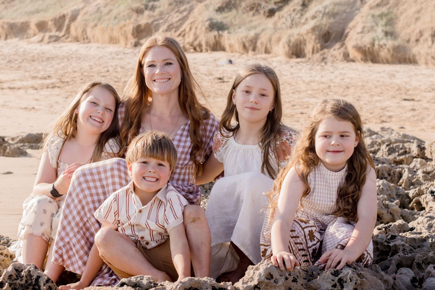 Group sitting together on coastal rocks wearing coordinated pink and gingham outfits on a sunny beach day.