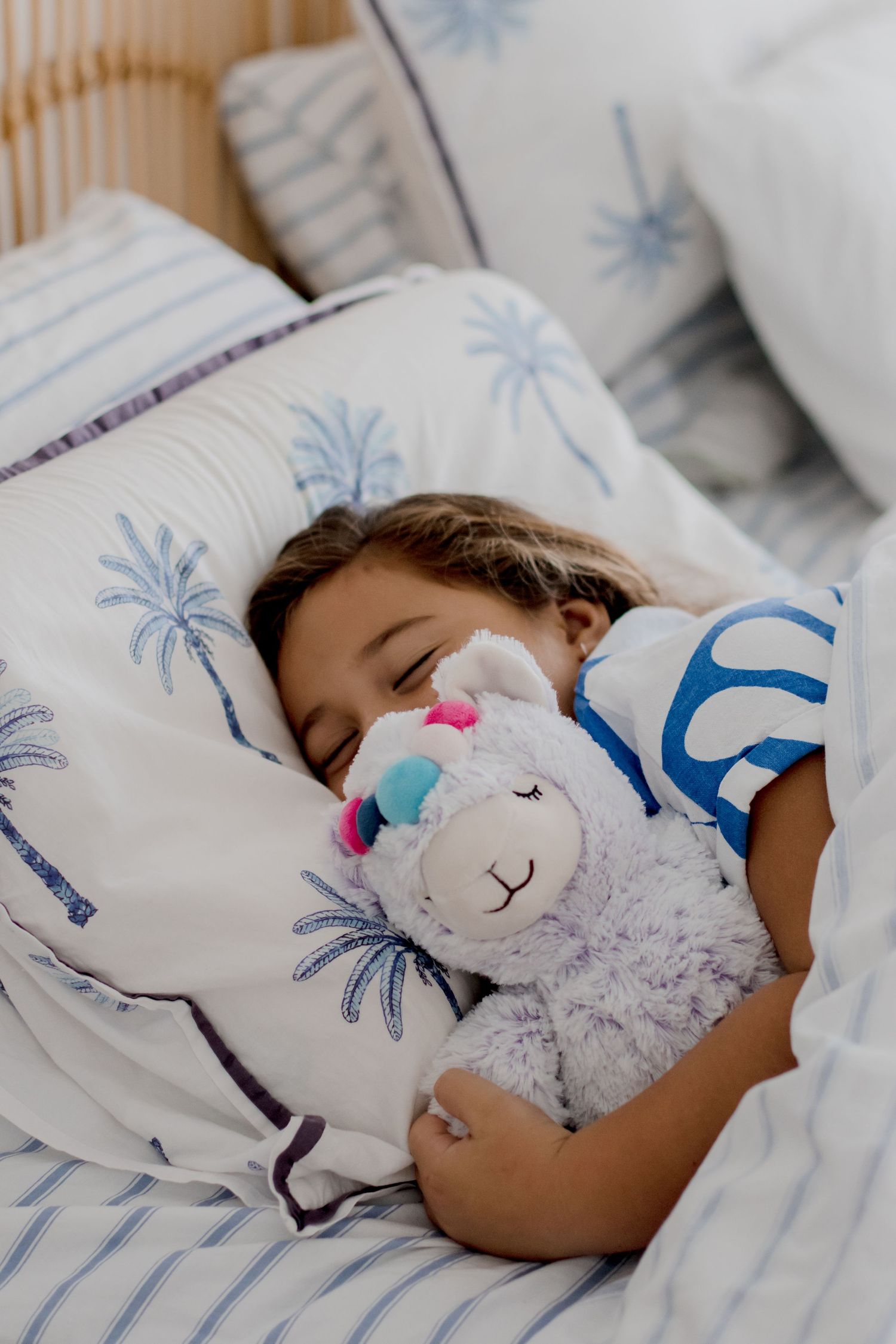 Sleeping peacefully with a stuffed animal on palm tree print bedding.