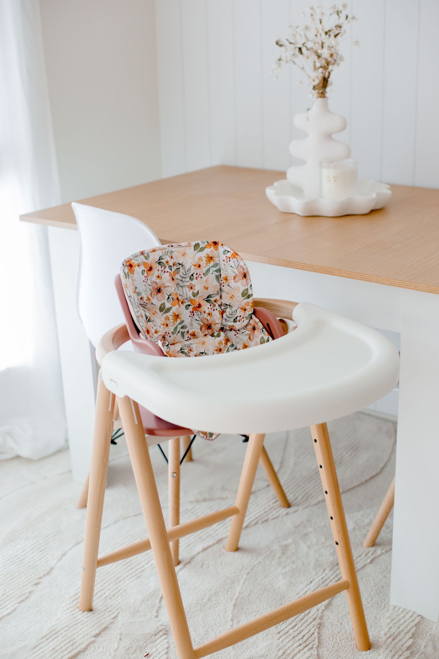 Modern white high chair with floral cushion insert and wooden legs.