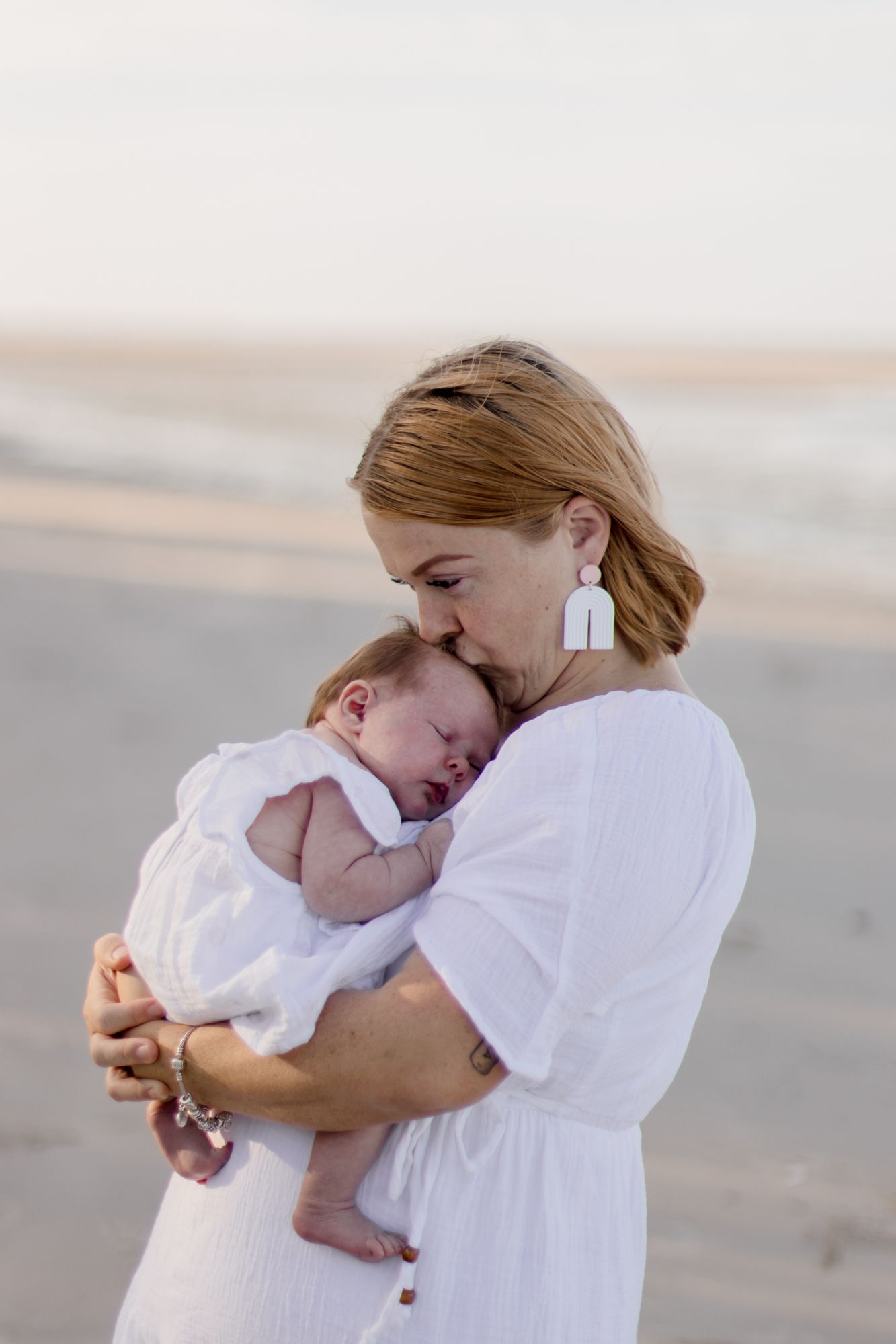A tender moment between mother and sleeping baby on a peaceful beach.