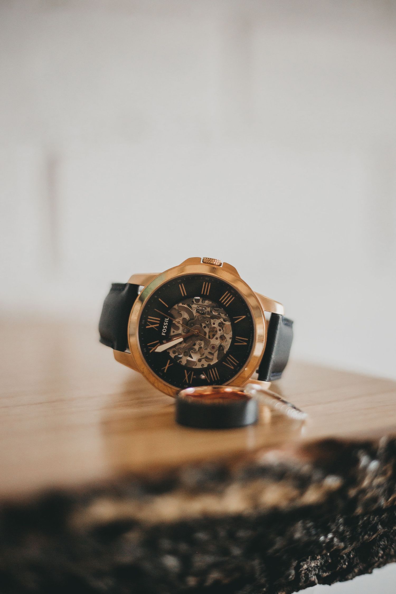 A luxurious rose gold and black skeleton watch with exposed mechanical movement shown at different angles on a wooden surface.