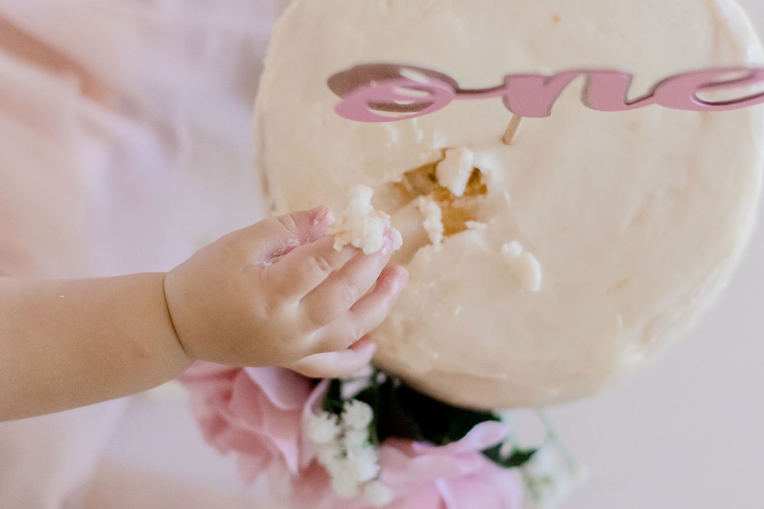 Detail shot of hands touching white birthday cake with pink decorative elements.