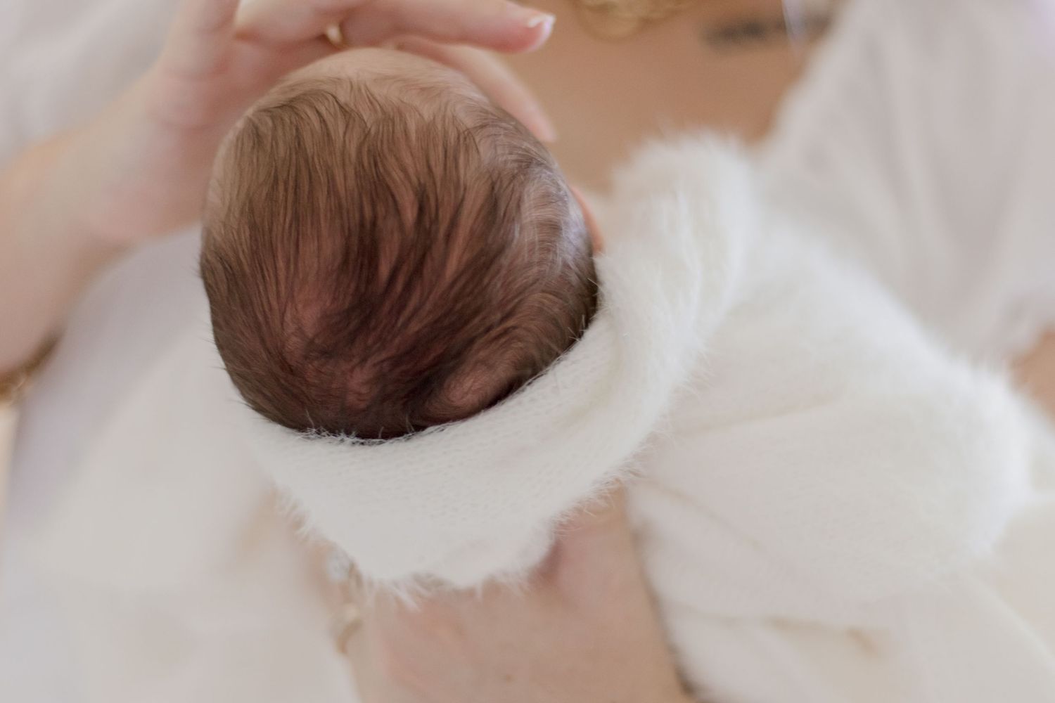Close up of newborn baby's head wrapped in soft white blanket.