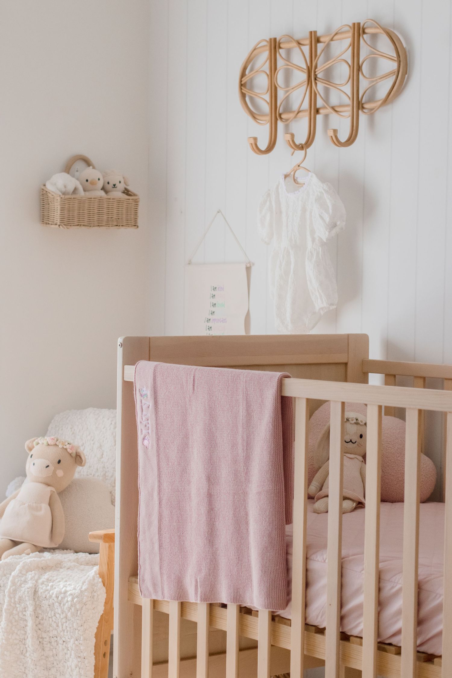 Neutral toned nursery with wooden crib, pink bedding, and decorative wall hangings.