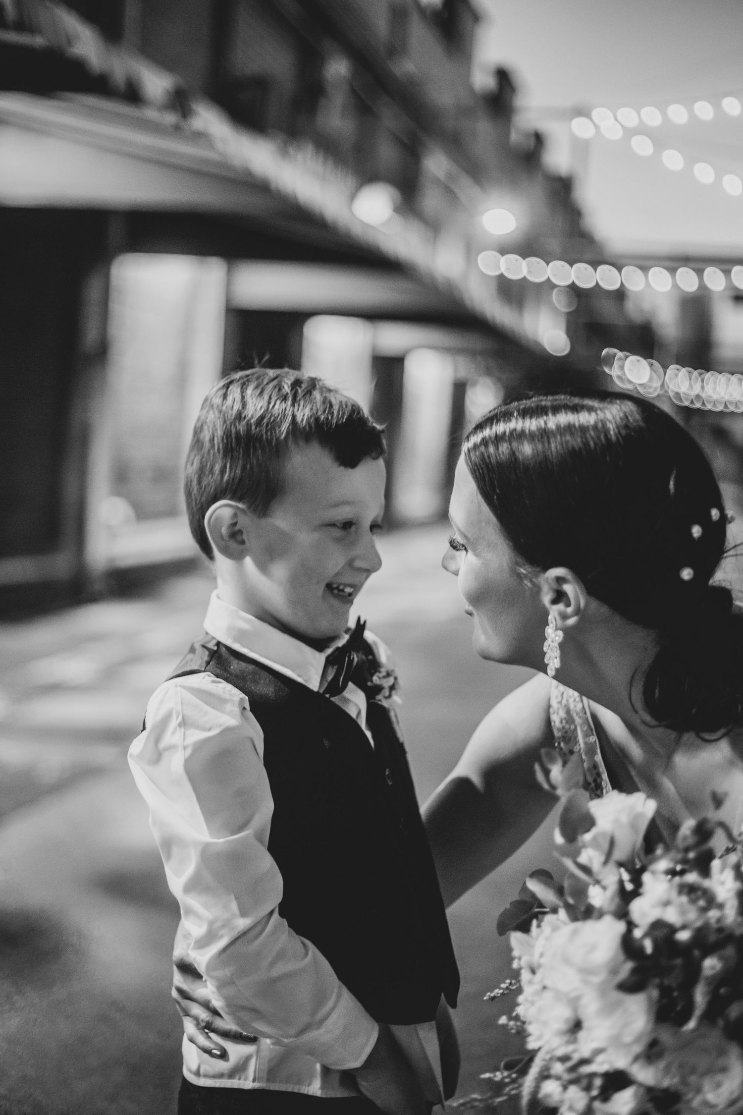 A black and white candid moment captured at a wedding reception with string lights and floral bouquet details.