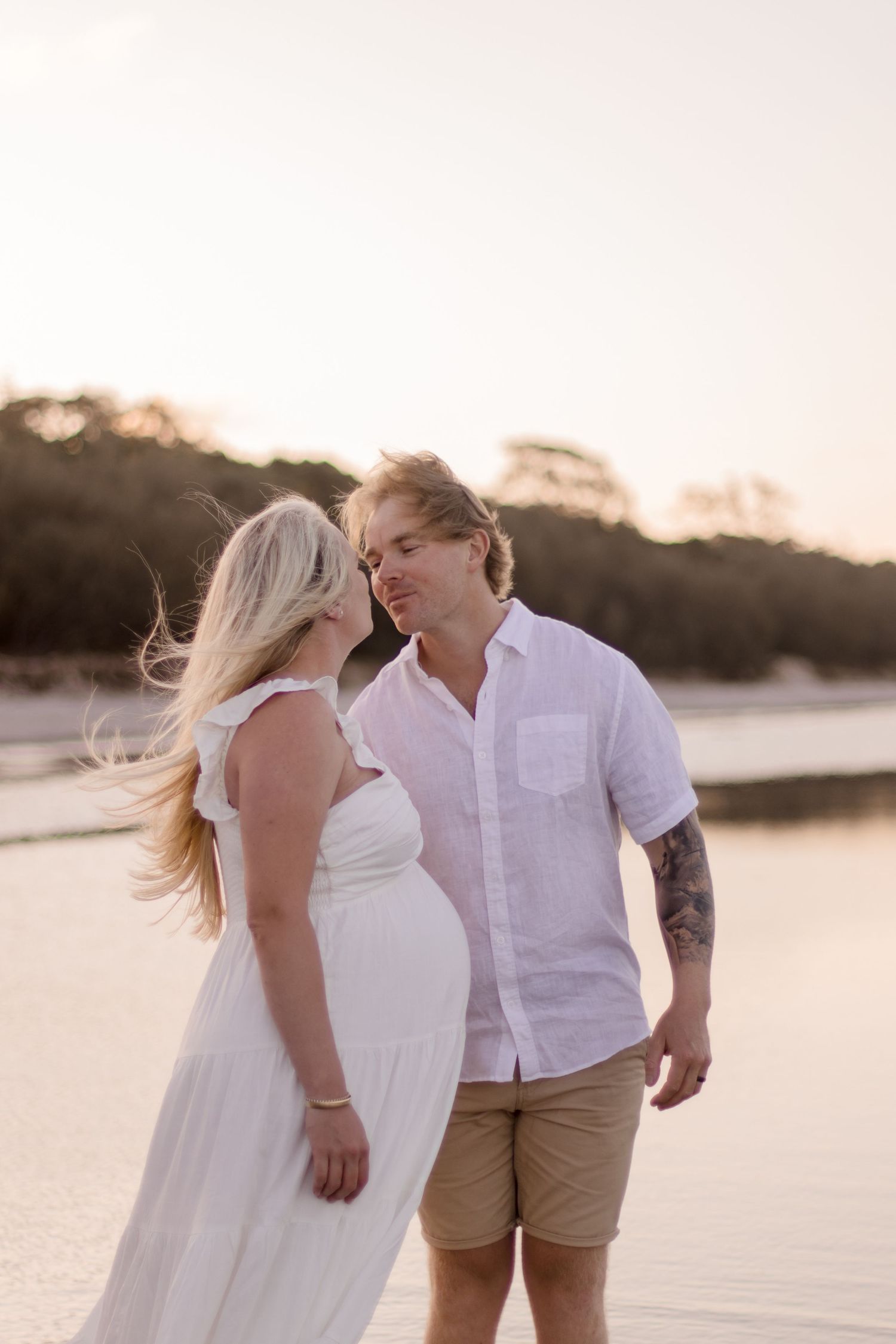 A tender moment between expecting parents during their beach photoshoot at sunset.