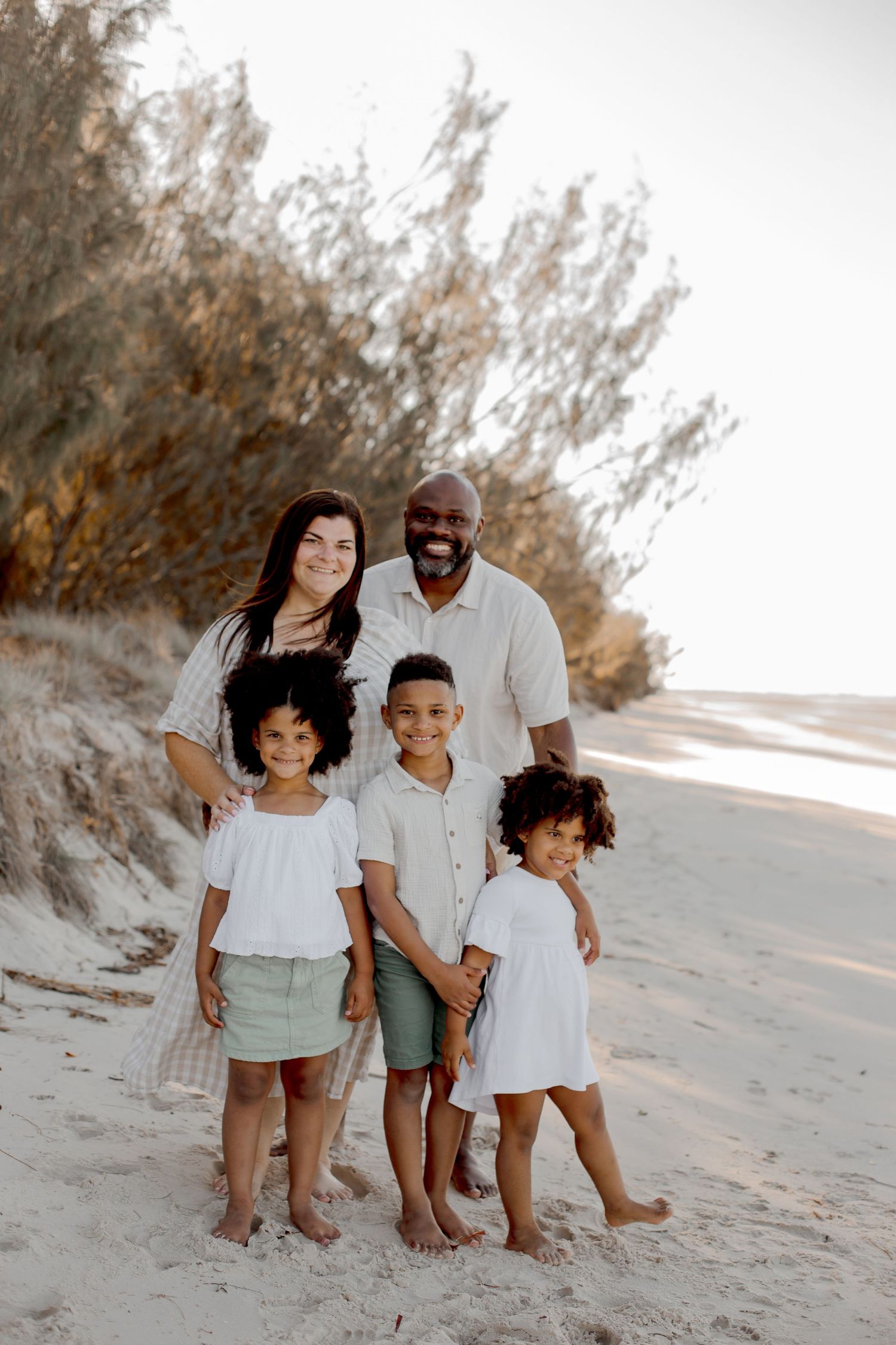 Family of five posing together on a beach with sand dunes in the background.