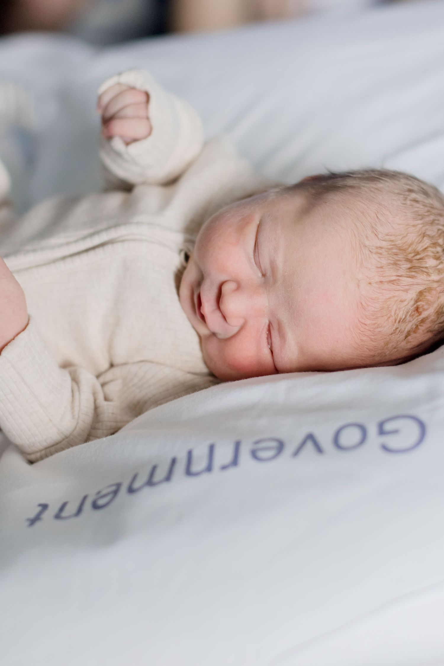 Sleeping newborn in cream-colored outfit resting on soft bedding.