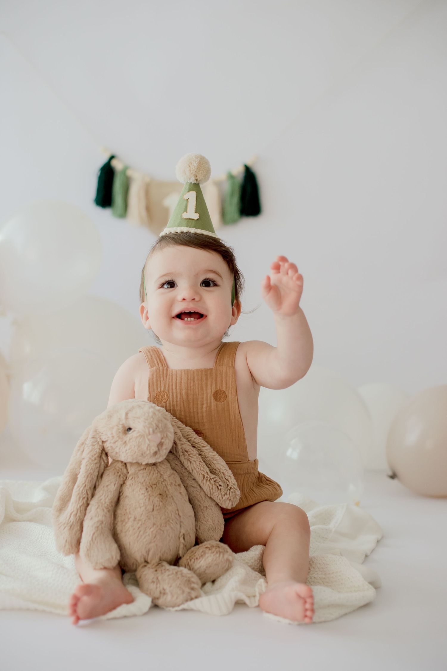 First birthday celebration setup with party hat, stuffed bunny, and white balloons.