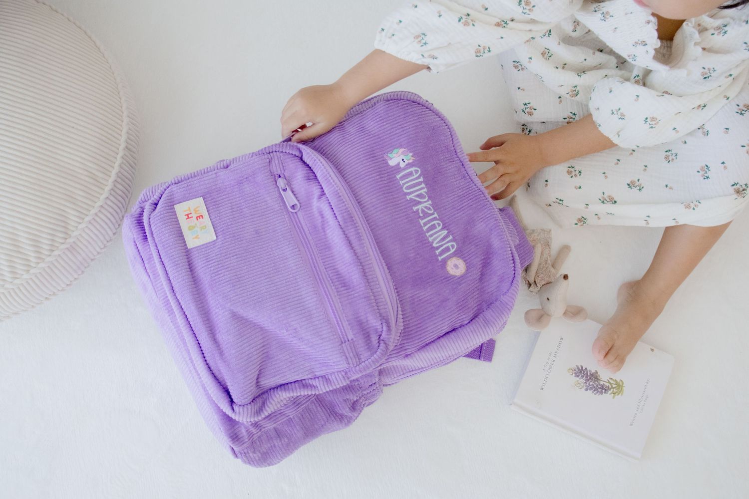 A light purple backpack with a zipper pocket being packed or organized on a white surface.