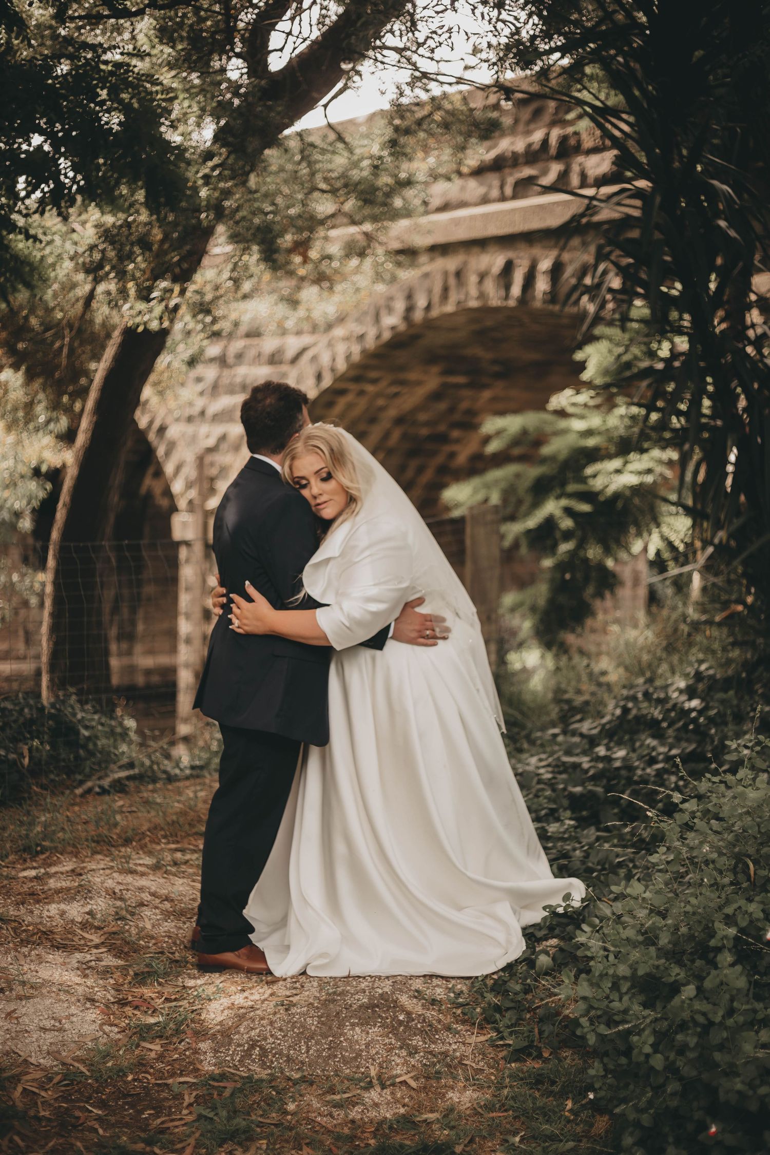 A wedding couple shares intimate moments in a series of romantic outdoor photos against a stone wall and garden setting.