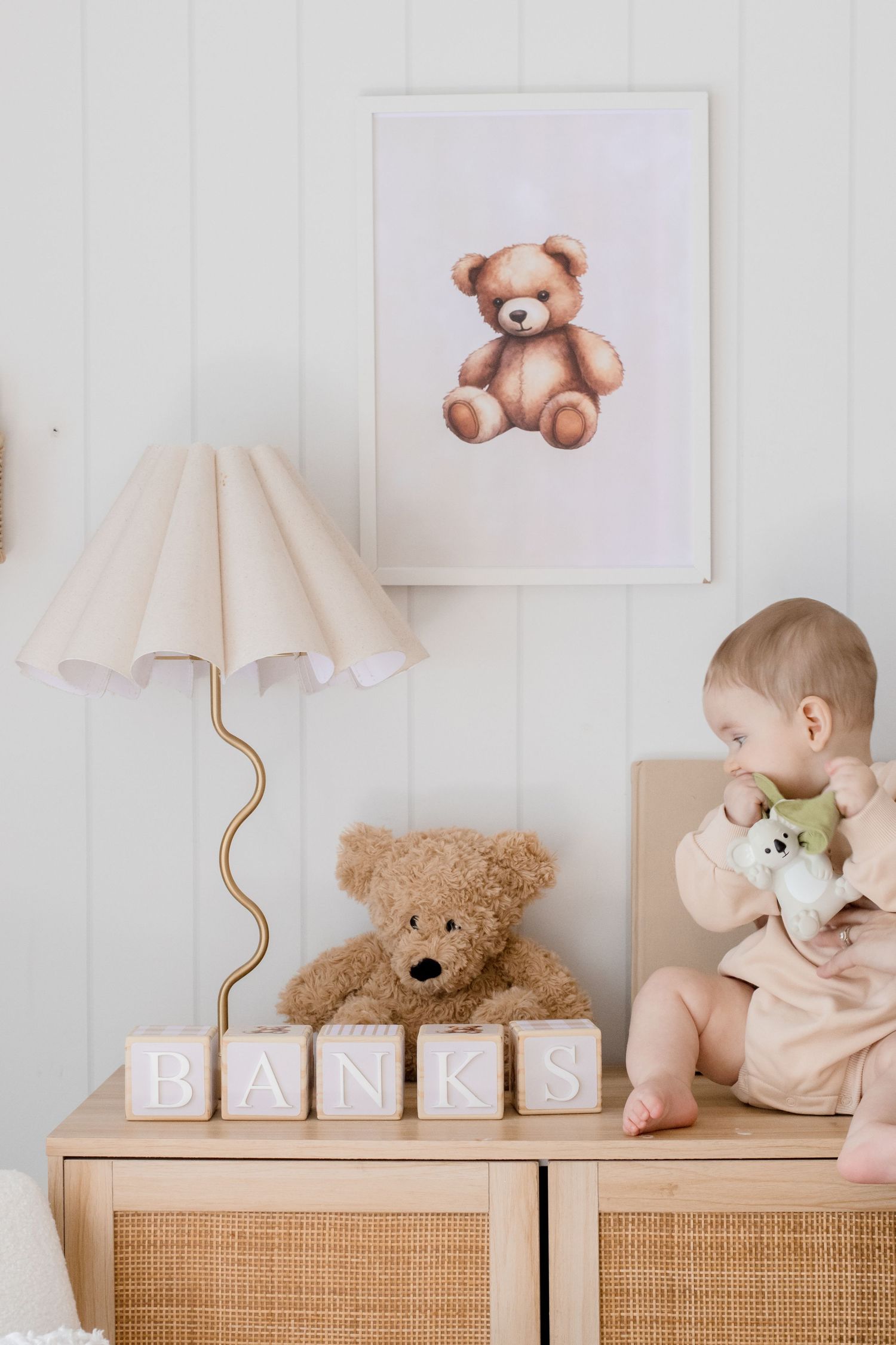 Multiple decorative teddy bears and stuffed animals arranged on top of wooden furniture against a white wall.