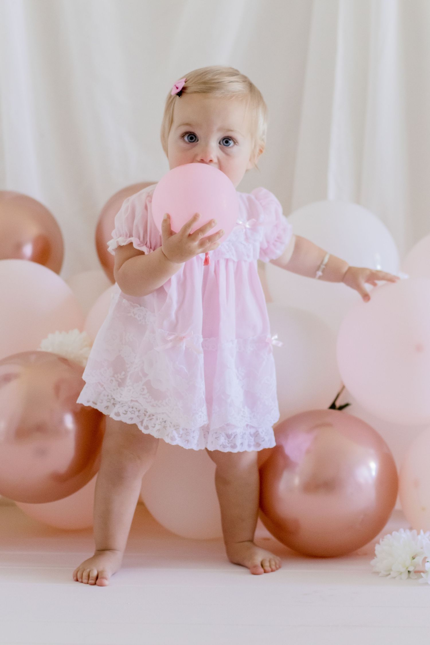 Toddler holding pink balloon to face while wearing delicate pink dress.