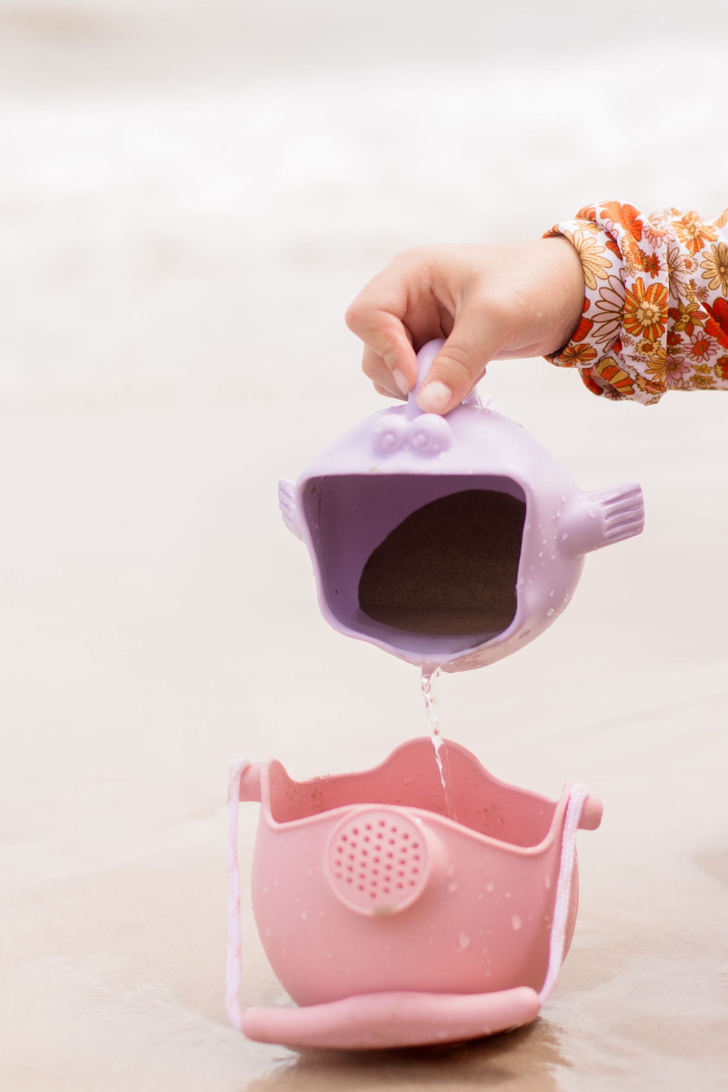 Purple whale-shaped watering toy pouring water into pink container.