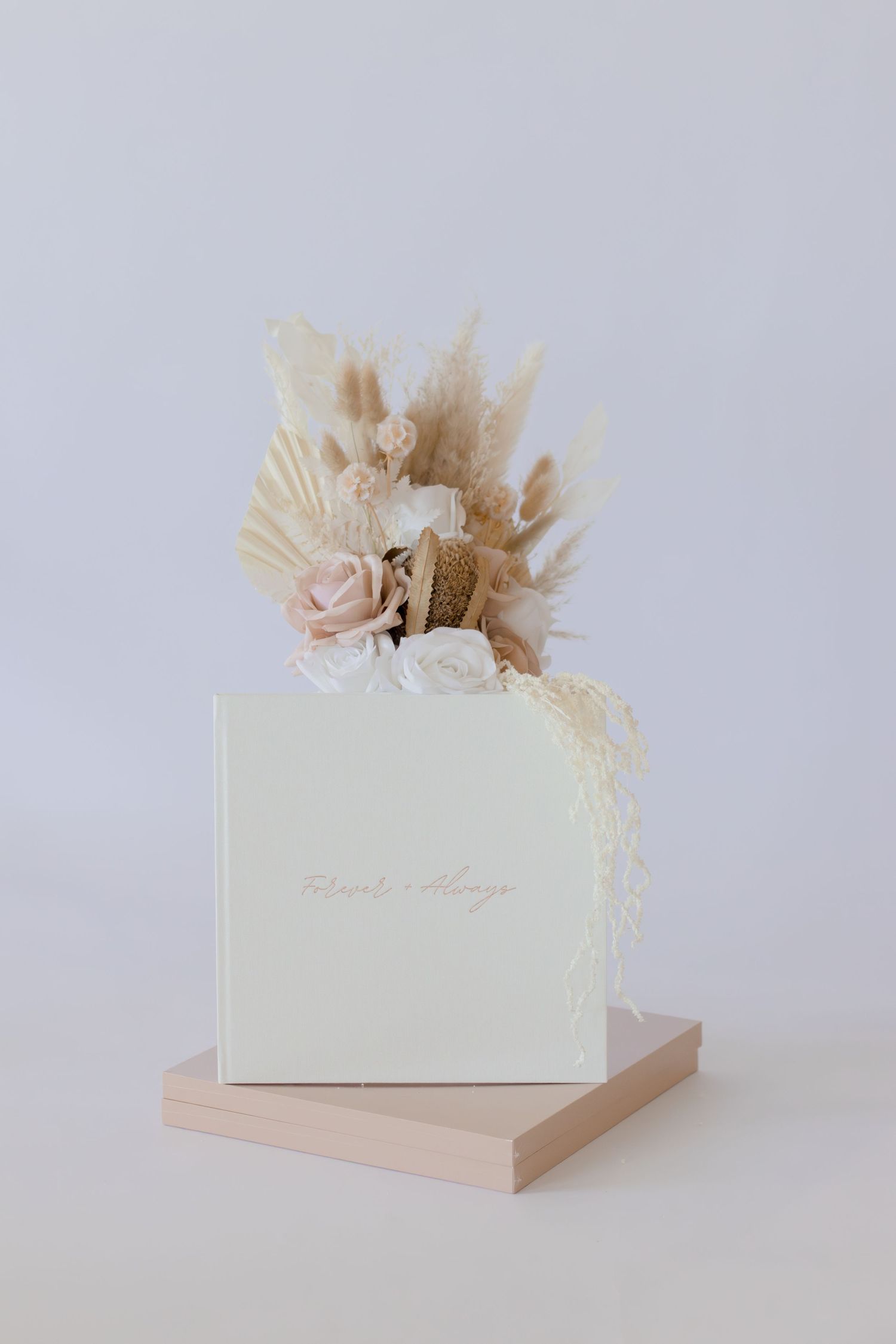 Elegant white gift box with dried pampas grass, blush roses, and lace floral arrangement on a soft pink platform.