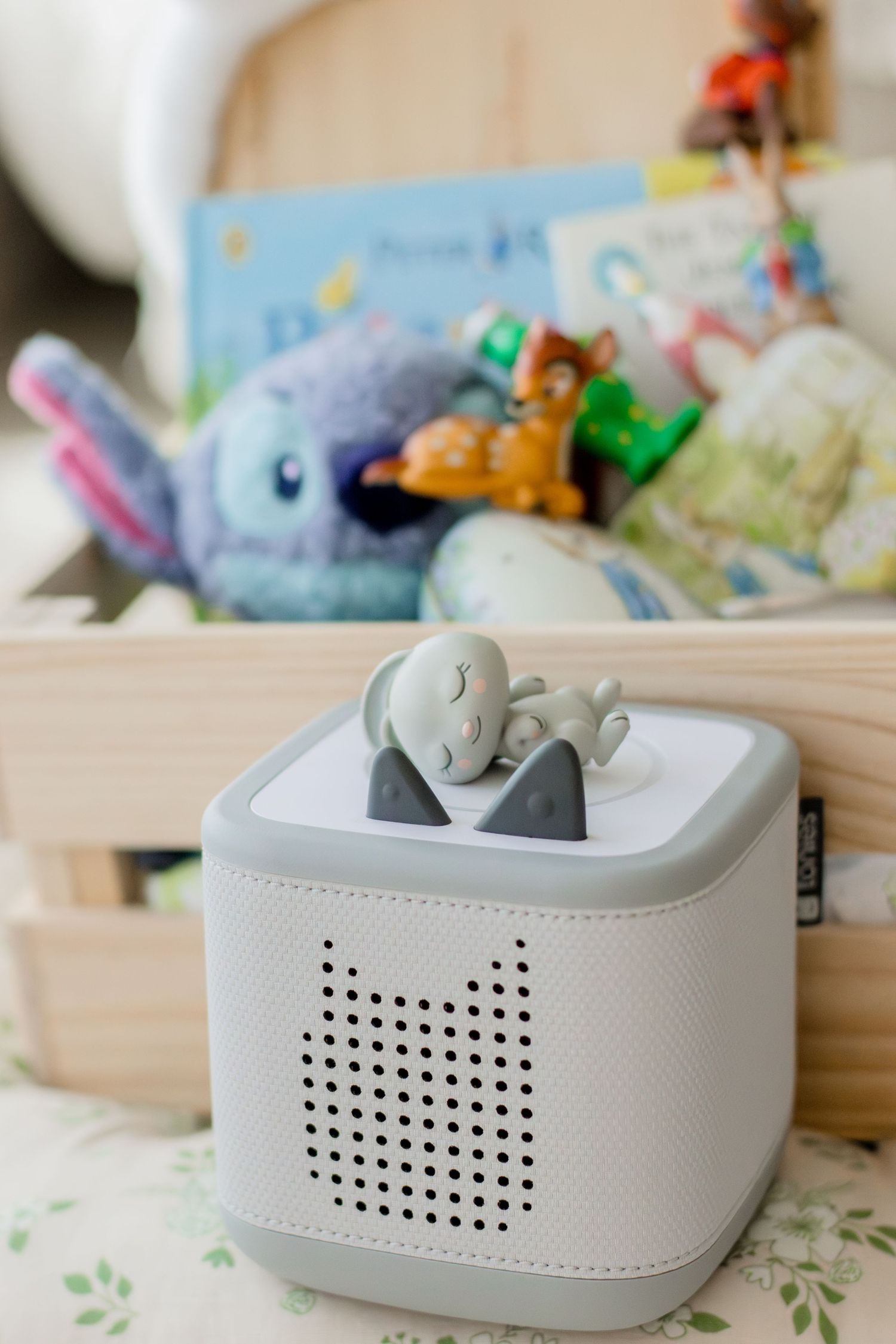 Toniebox audio player with a turtle Tonie figurine on top, displayed in front of a basket of children's toys and books.