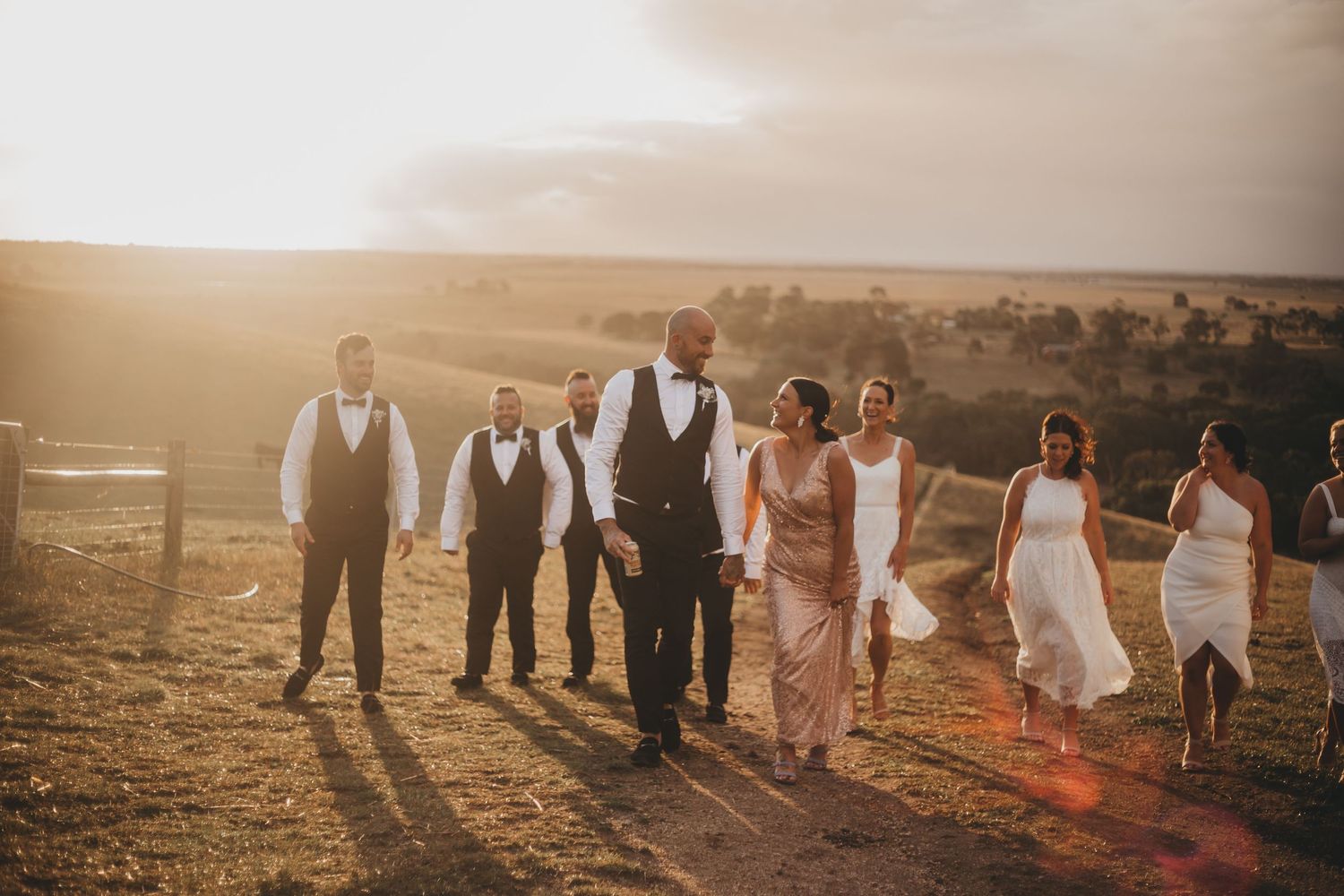 Silhouettes of wedding party group pose against a sunlit outdoor landscape during golden hour sunset.
