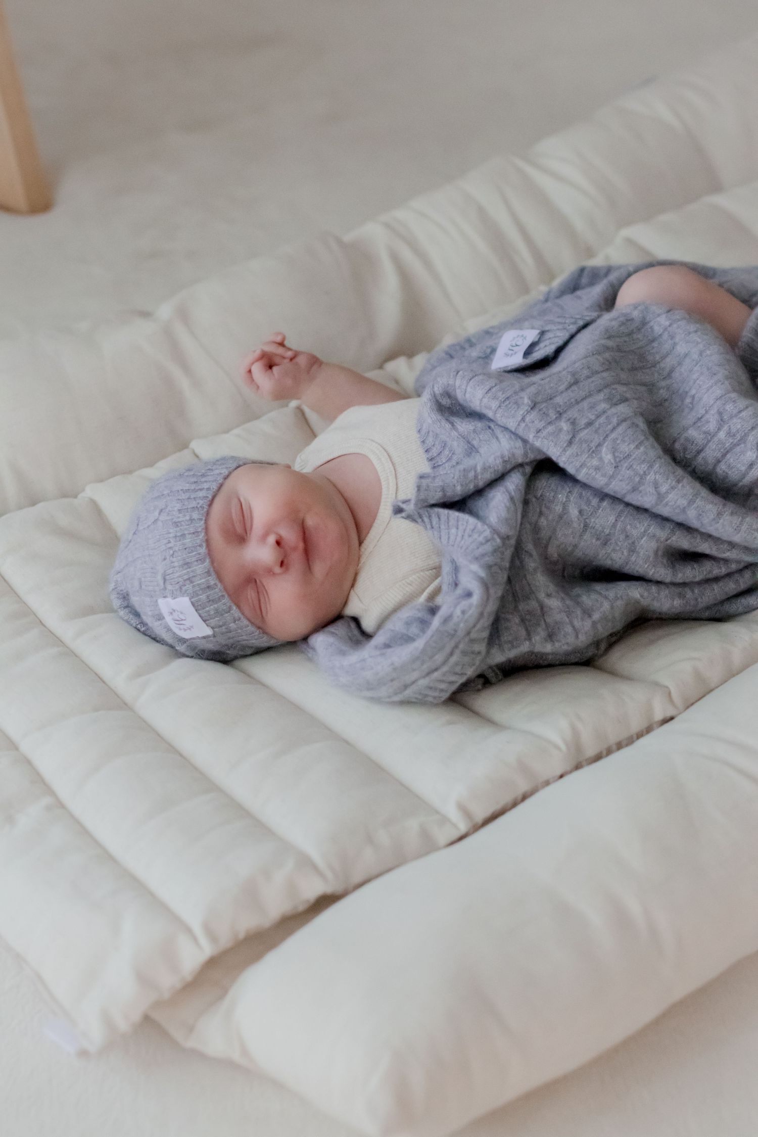Baby dressed in cozy grey knitwear resting on white bedding.